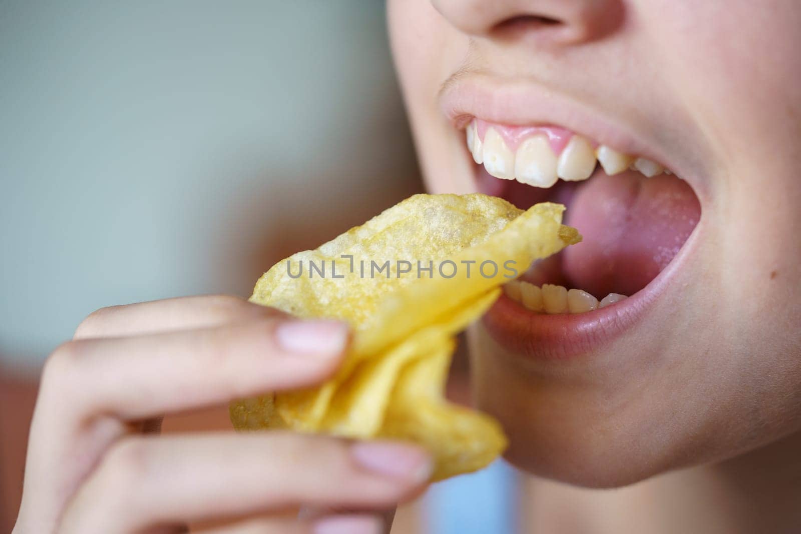 Crop unrecognizable teenage girl with mouth wide open eating crunchy potato chips at home