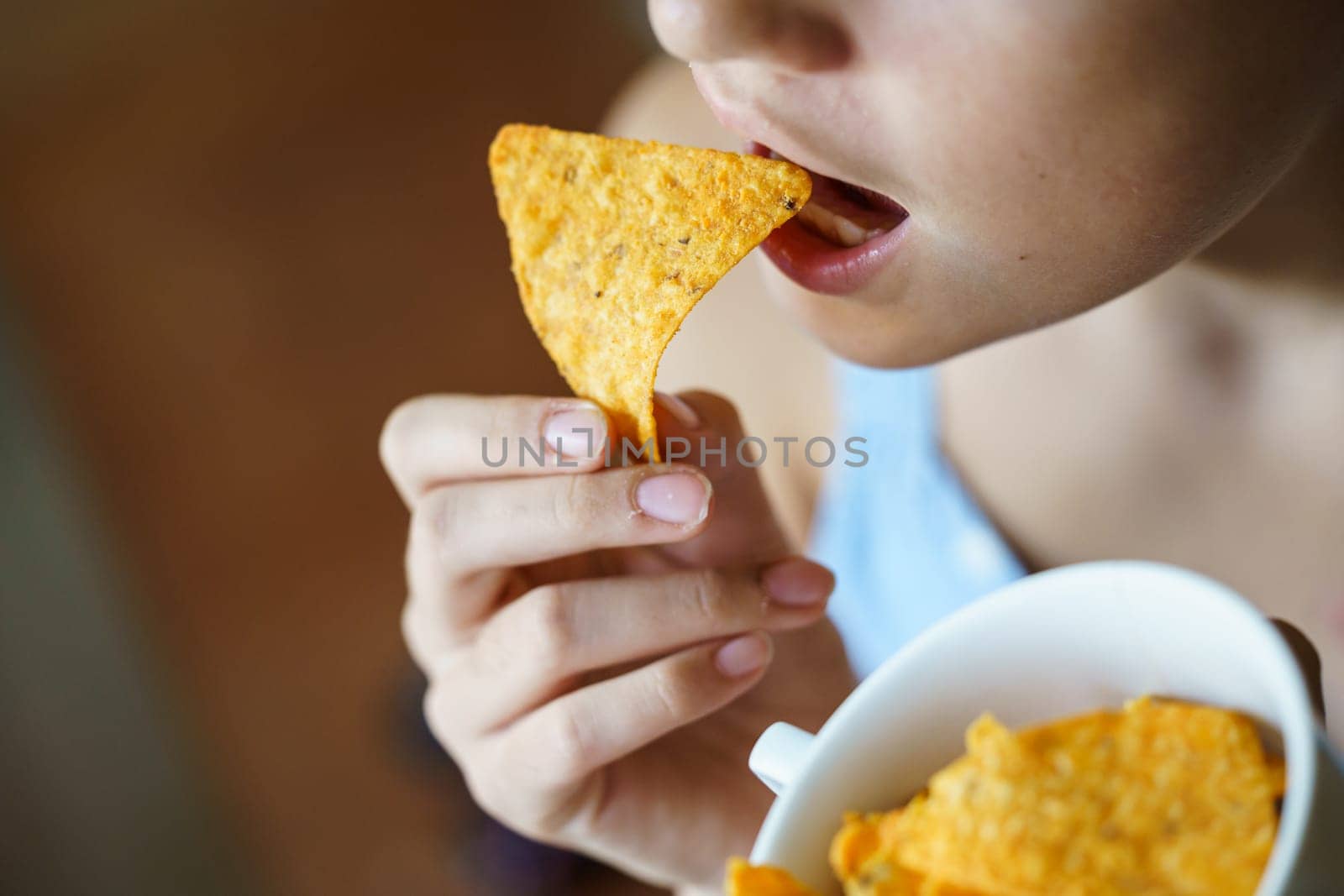 From above of crop unrecognizable teenage girl eating delicious Mexican nacho chip at home