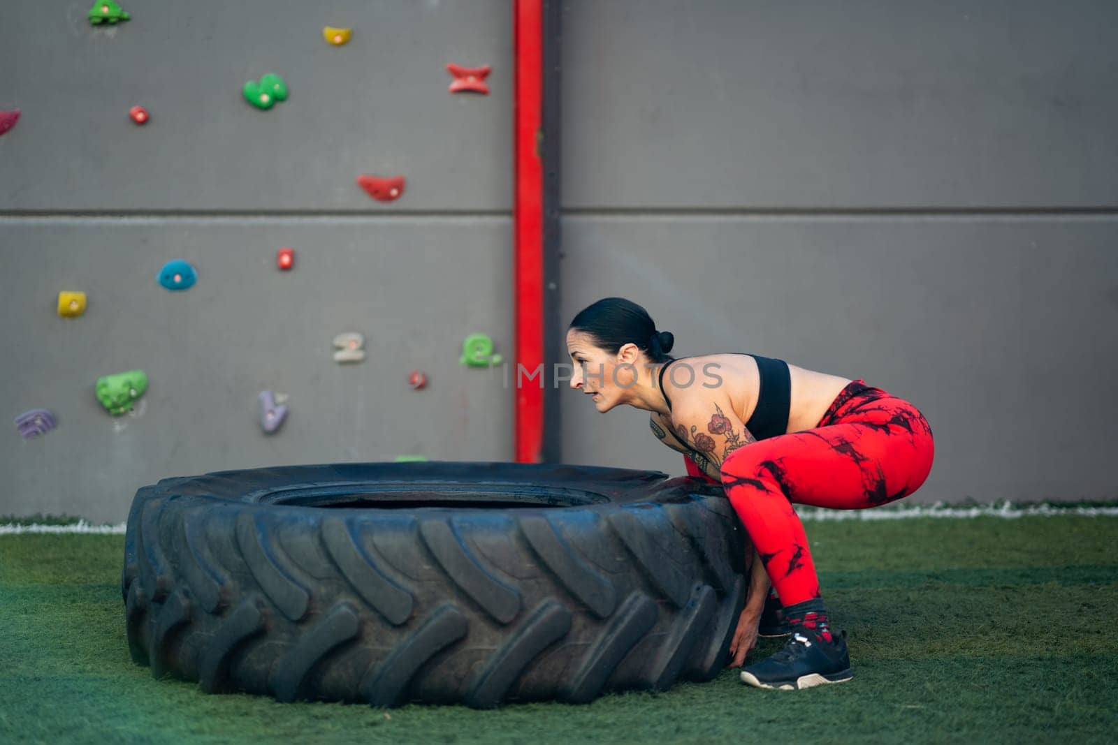 Side view of a mature sportive woman lifting a truck wheel in a gym