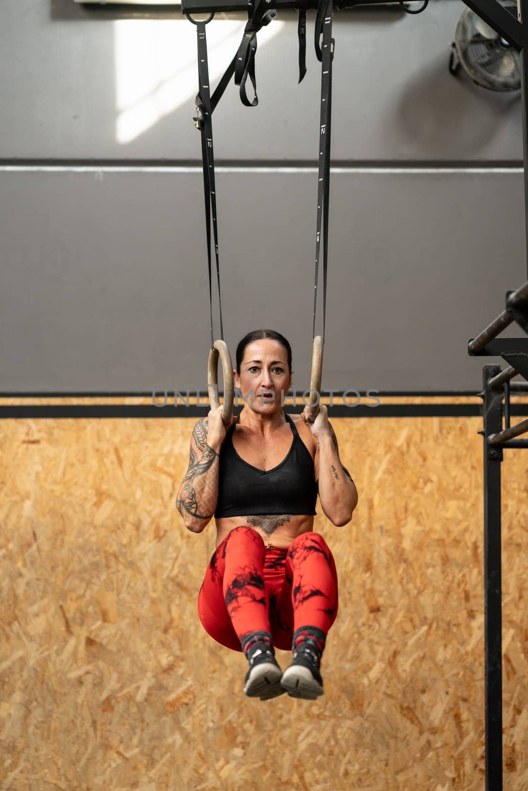Vertical photo of a mature sportive and strong woman training with olympic rings in a cross training center