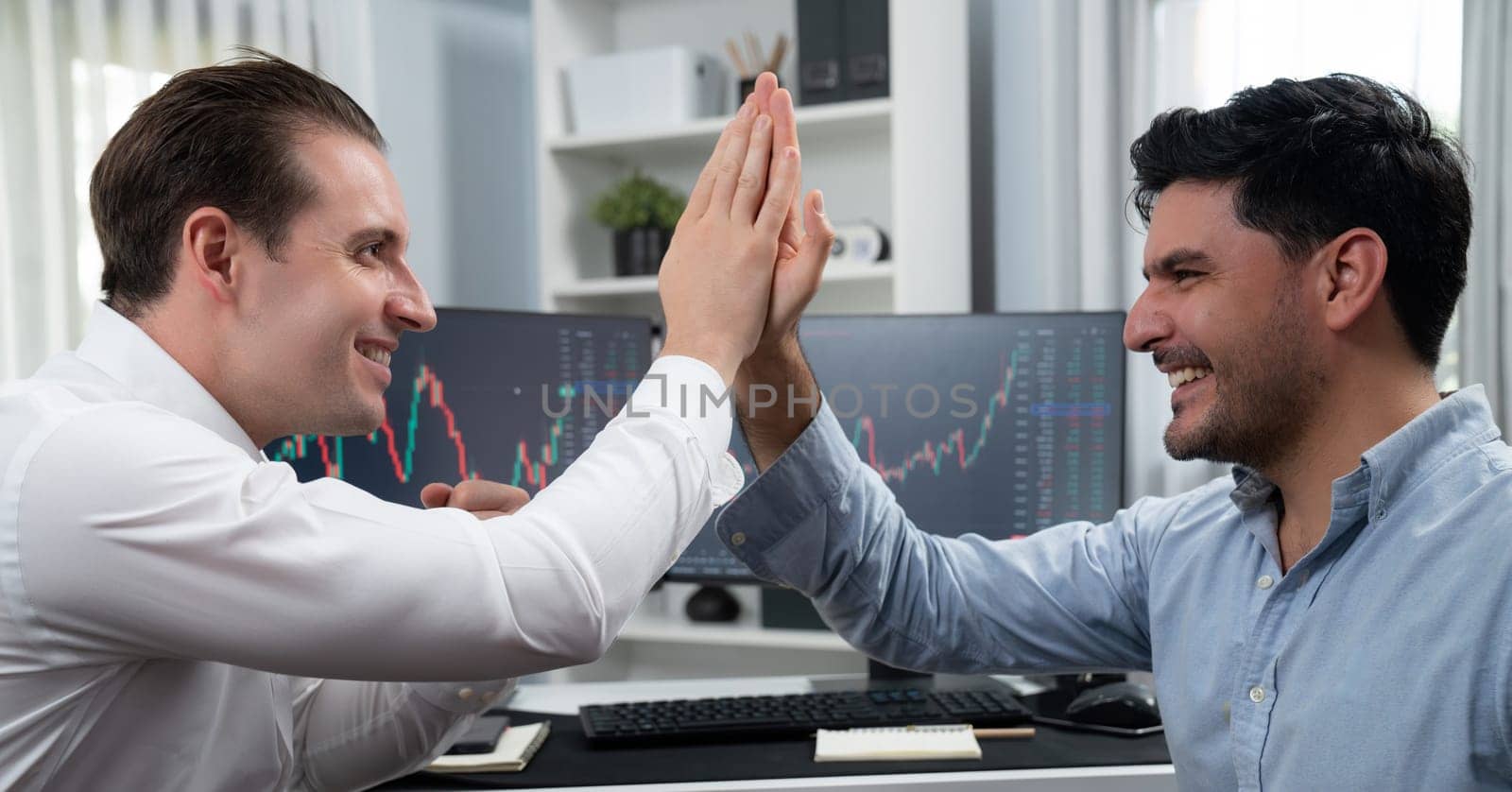 Cheerful two smiling stock traders giving high five on panorama view to success of digital technology in dynamic data monitor background. Achievement investors in business at workplace. Sellable.