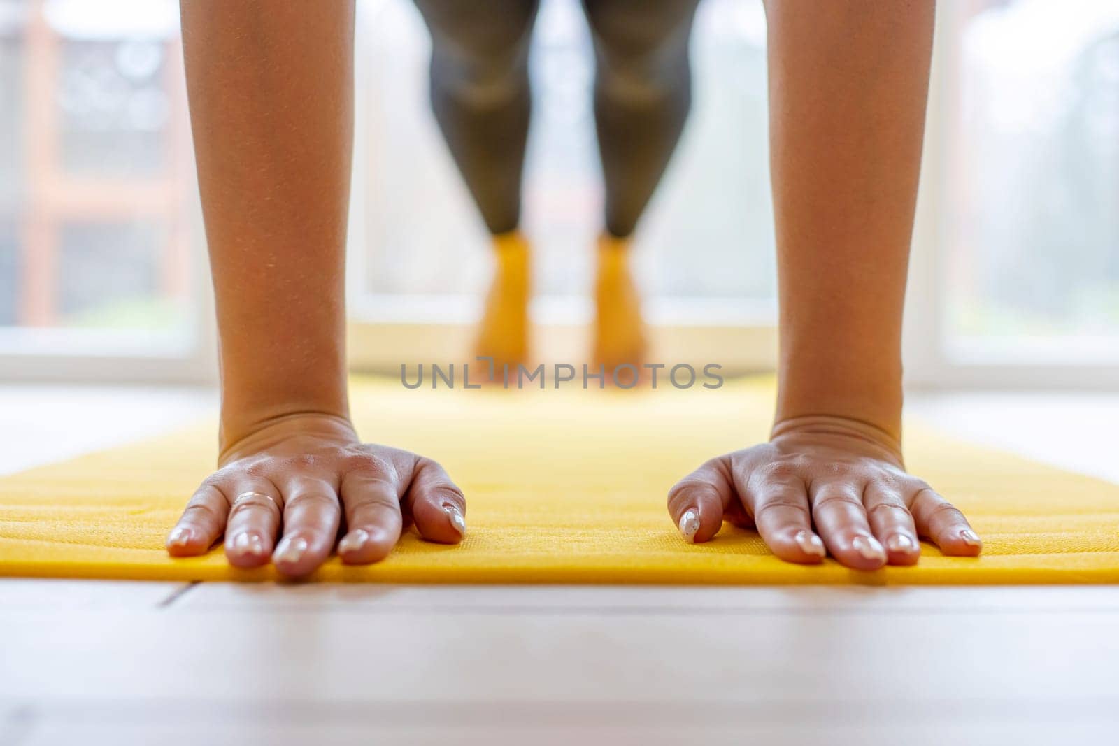 Hands pressed flat on yellow yoga mat, workout session indoors by andreyz