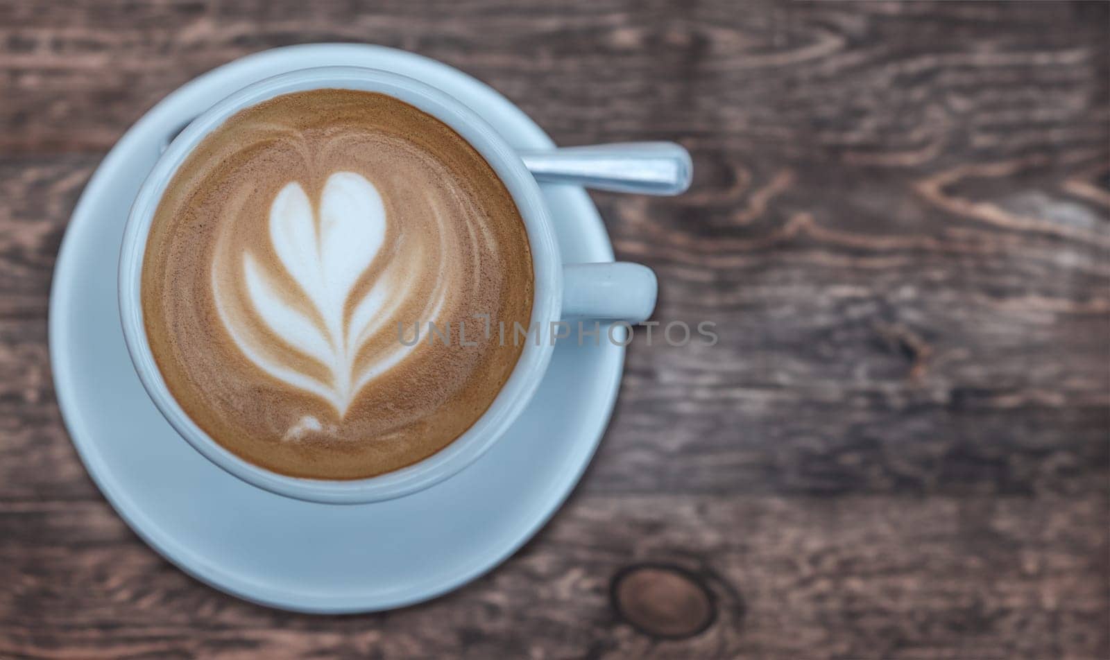 A Cup Of Coffee, Complete With Latte Art In The Frothy Milk, On A Rustic Cafe Table WIth Copy Space