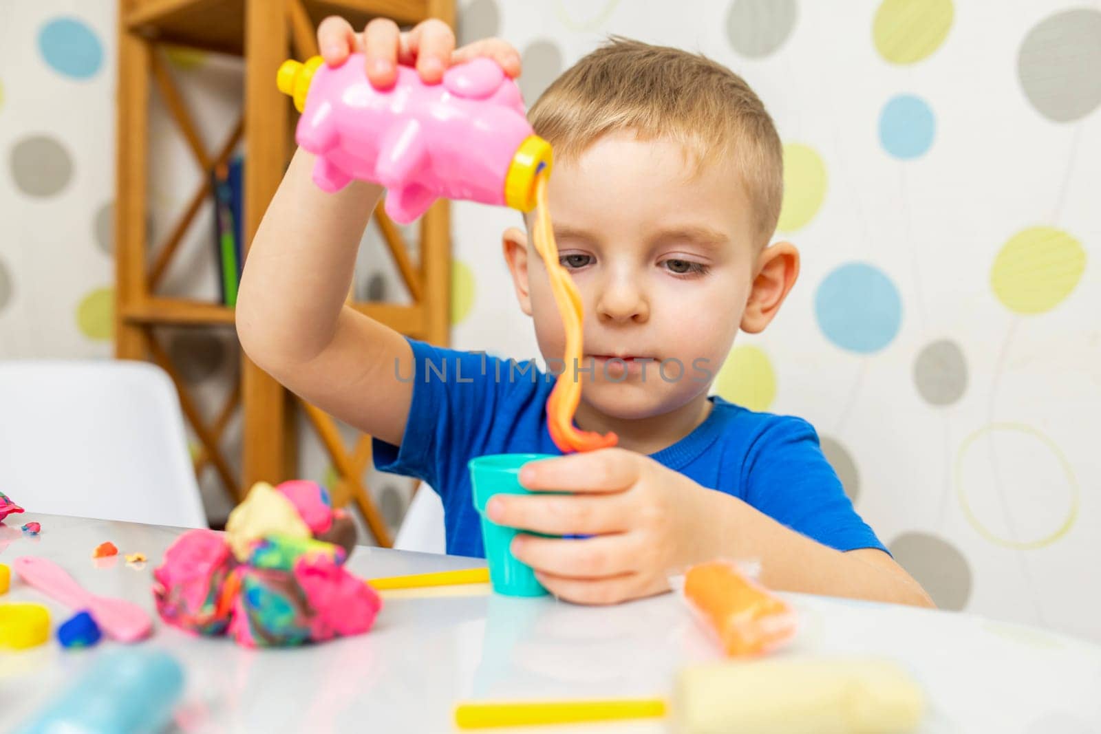 Kid playing with play dough. Cute child sitting at the table and plays with playdough. Creative leisure activity concept.