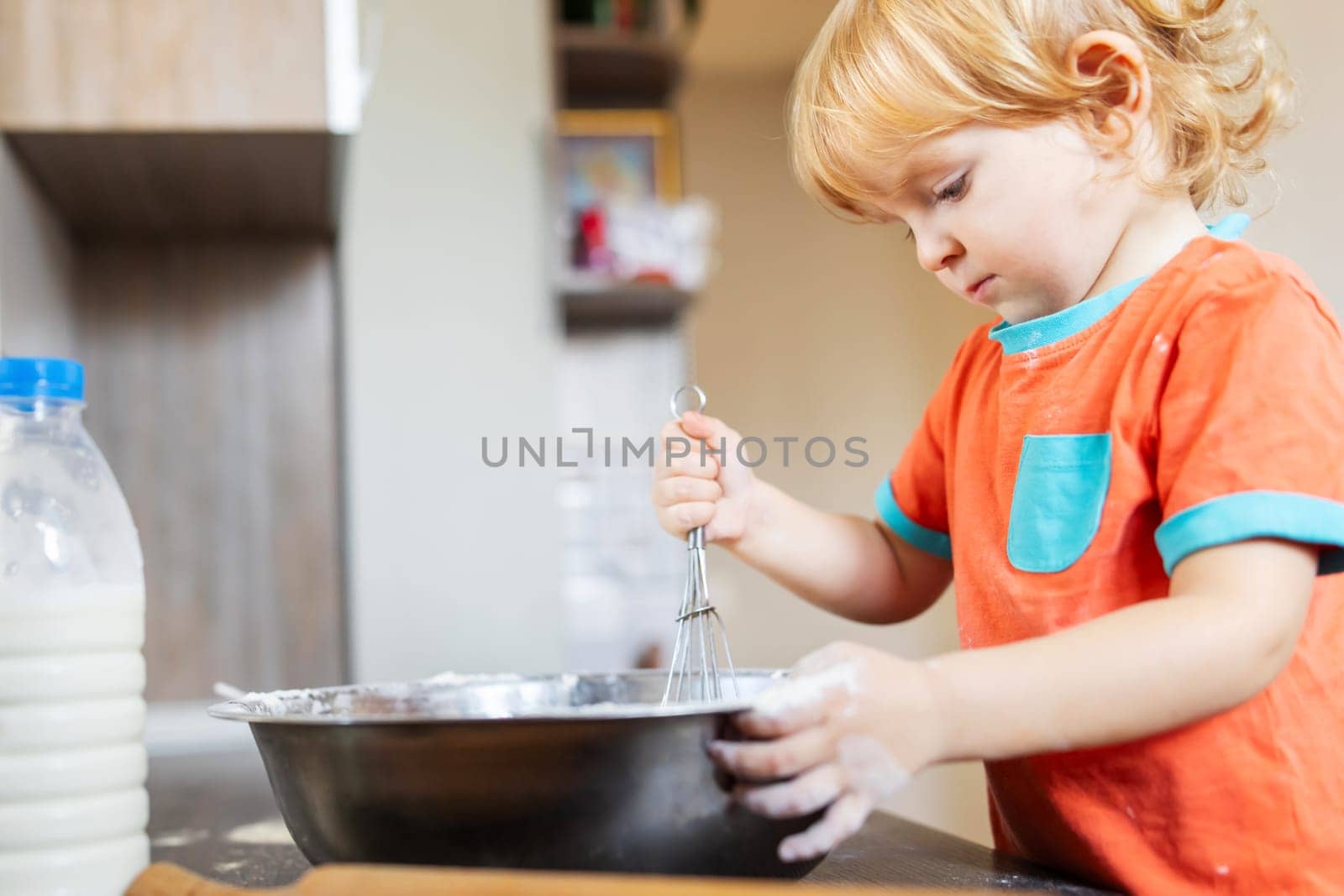 Cute little boy makes baking dough in the kitchen at home.