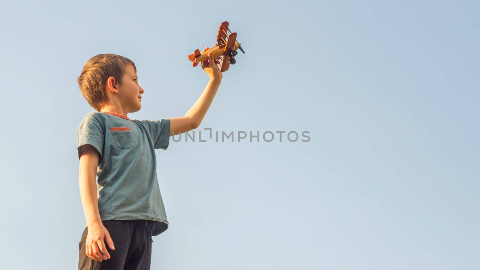 Happy kid playing with toy wooden airplane against sky background. Concept of educations, future, business, international and travel