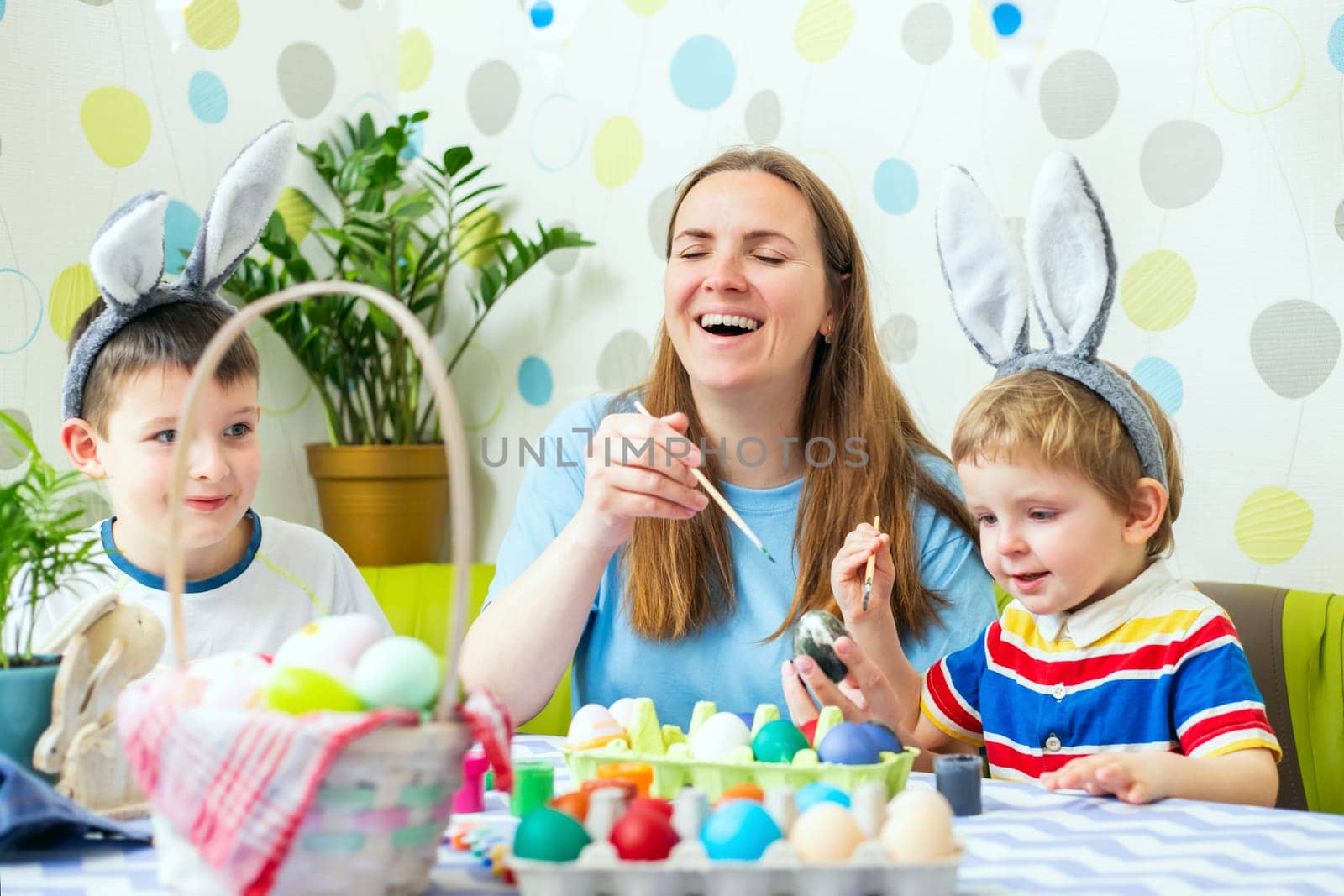 Happy Easter. A mother and her children painting Easter eggs. Happy family getting ready for Easter. Cute boys wearing bunny ears on Easter day