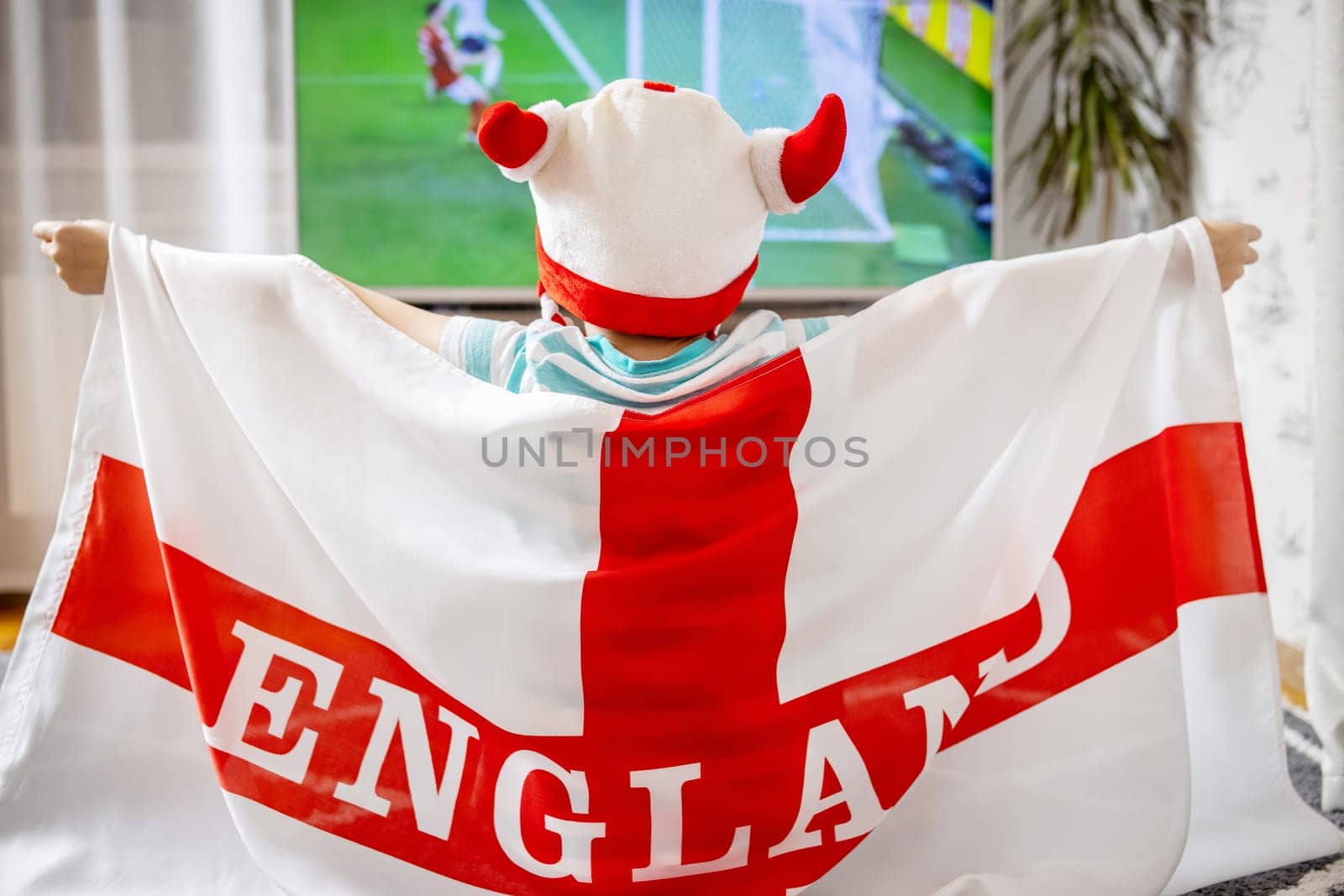 A boy with England flag watching soccer game on TV and supporting his national football team