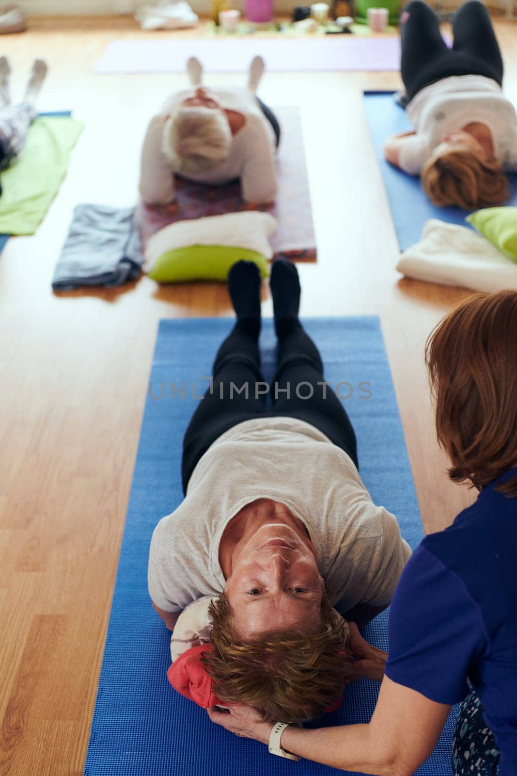 Top view of group of senior women engage in various yoga exercises, including neck, back, and leg stretches, under the guidance of a trainer in a sunlit space, promoting well-being and harmony.