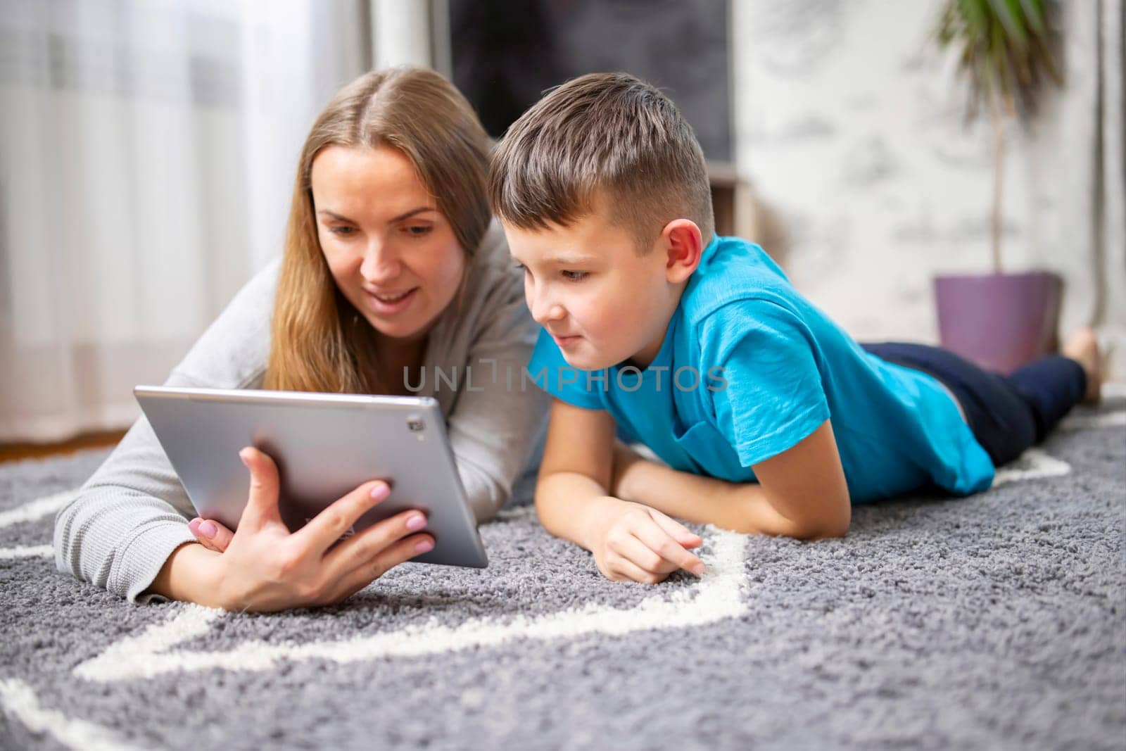 Happy loving family. Young mother and her son using tablet pc lying on carpet. Funny mom and lovely child are having fun at home