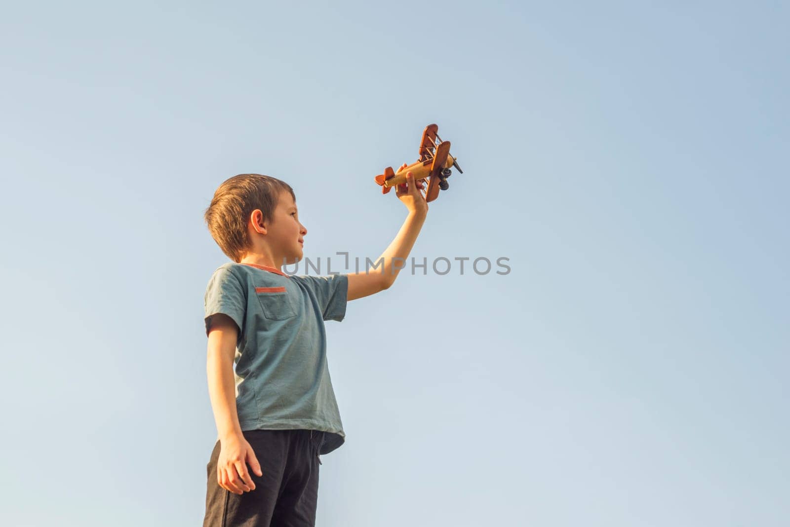 Happy kid playing with toy wooden airplane against sky background. Concept of educations, future, business, international and travel