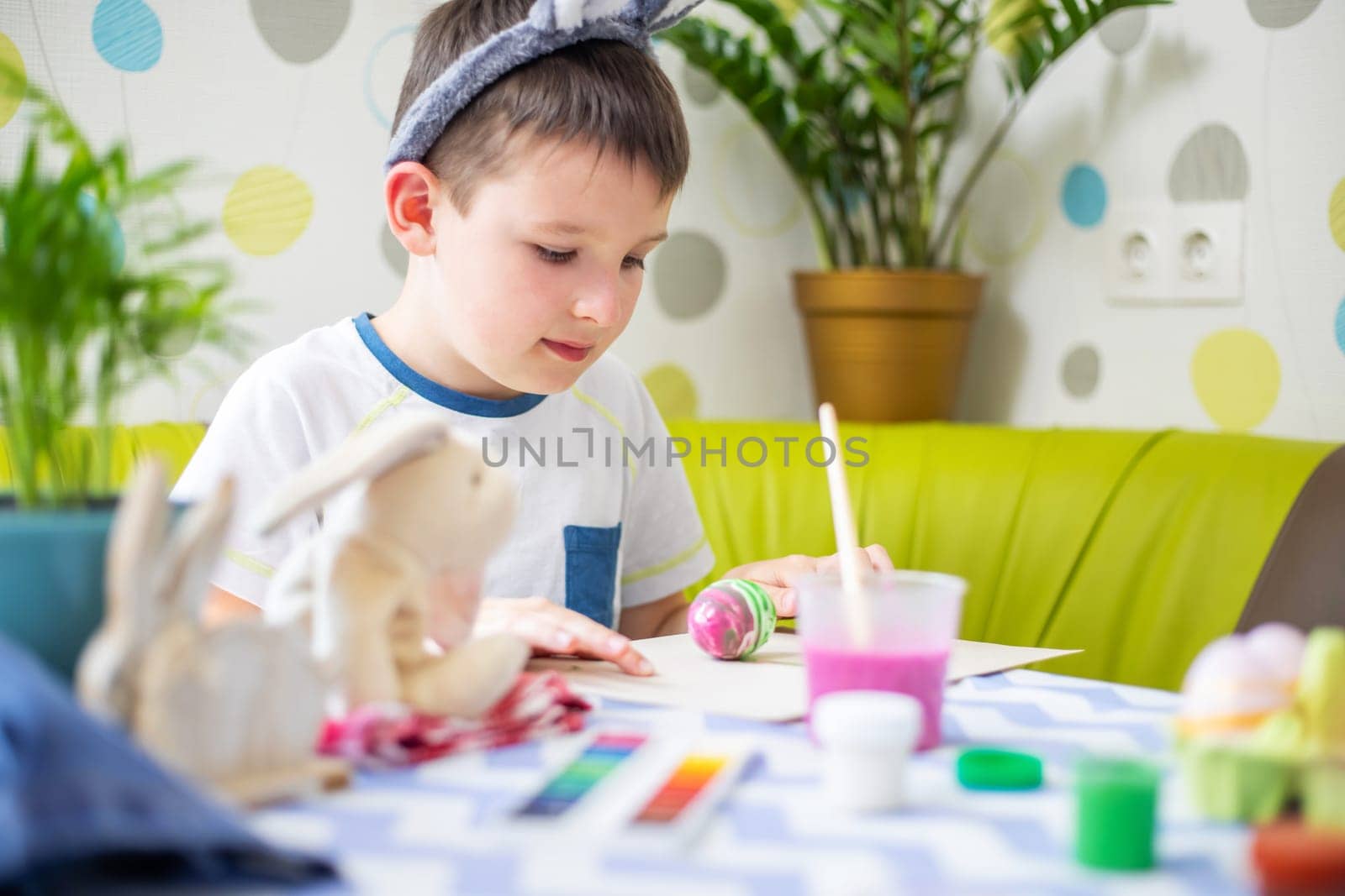 Happy Easter. Kid is dyeing Easter eggs. Boy in bunny ears dyes colorful egg for Easter hunt