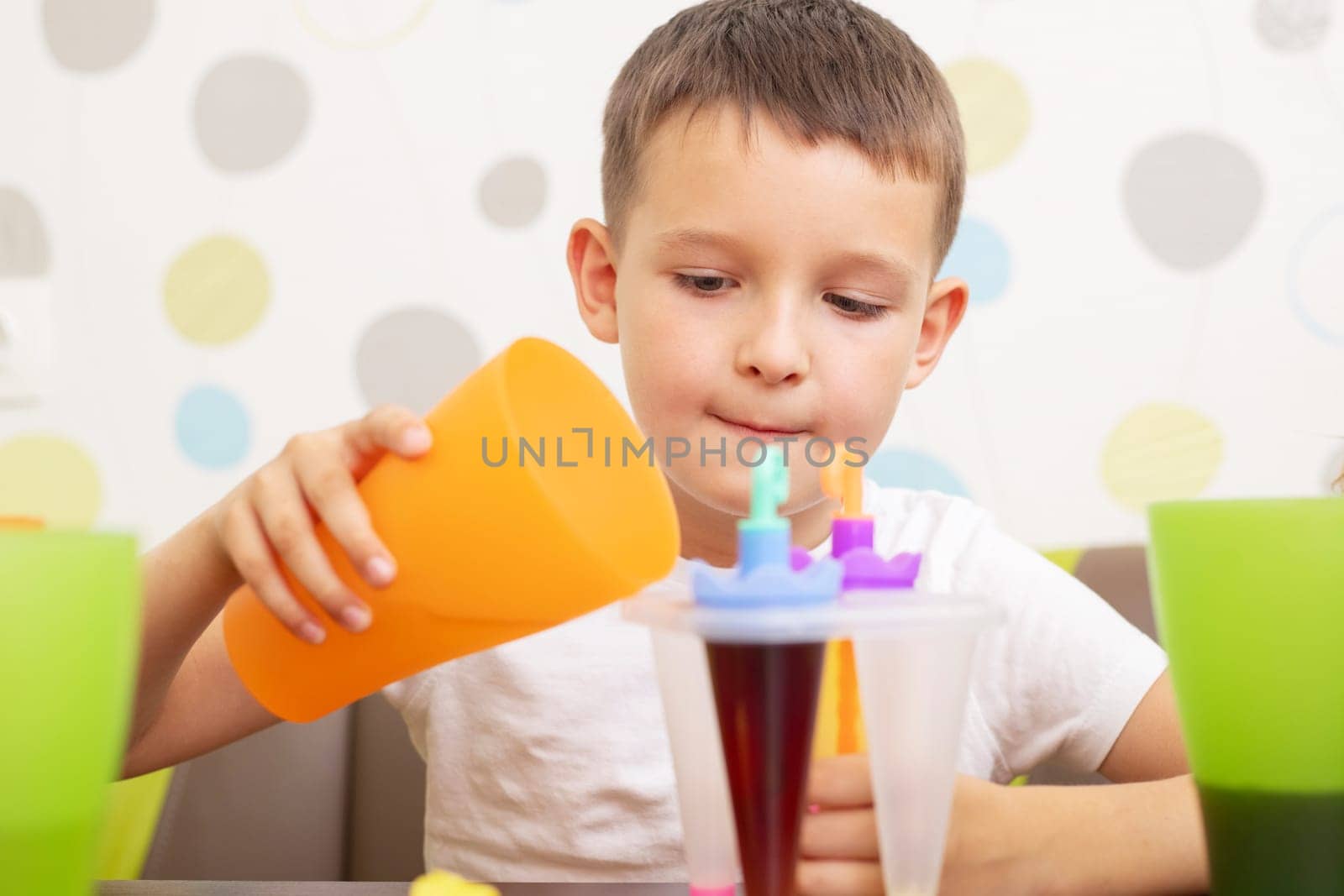 Child making ice cream from fruit juice on table at home.