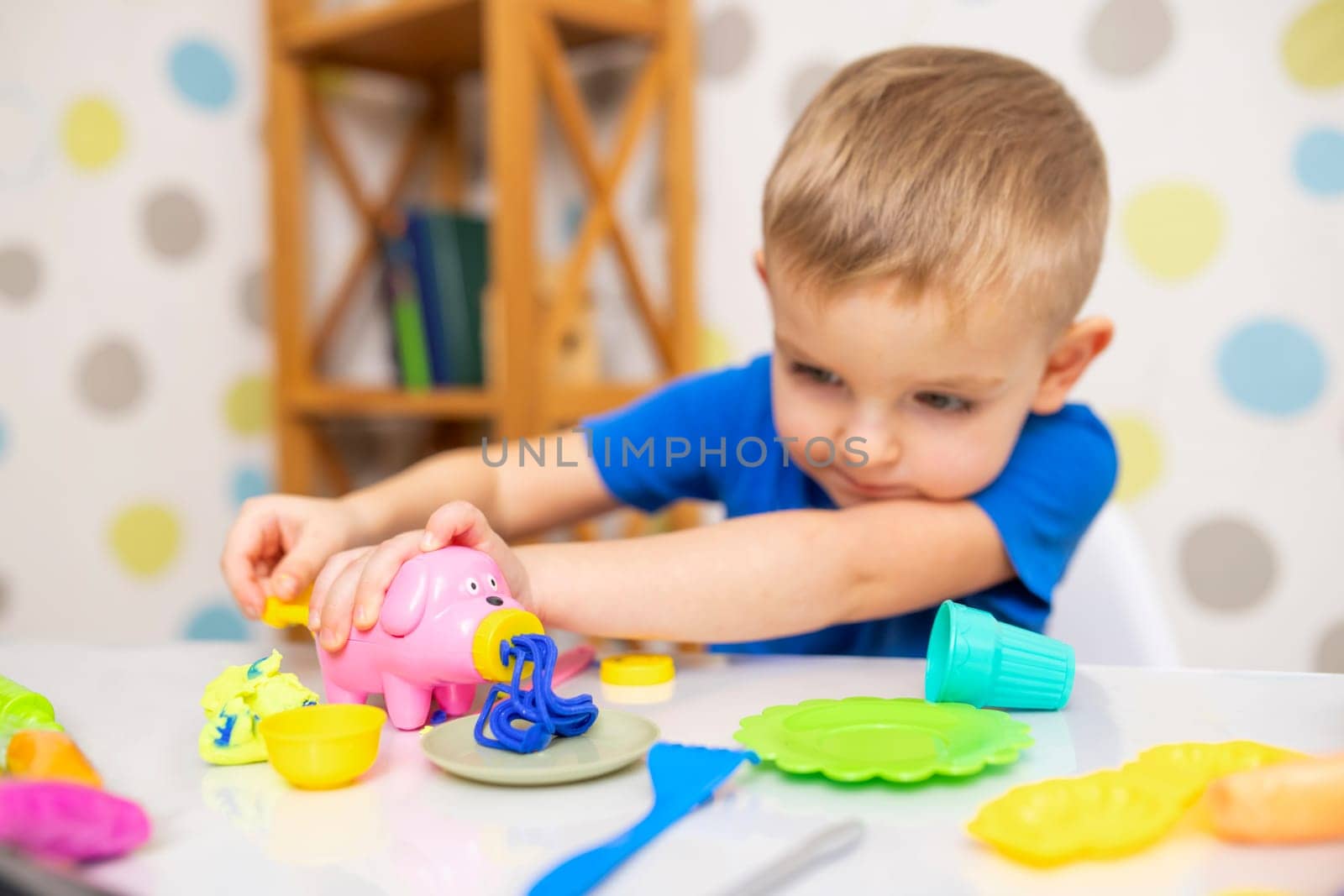 Kid playing with play dough. Cute child sitting at the table and plays with playdough. Creative leisure activity concept.