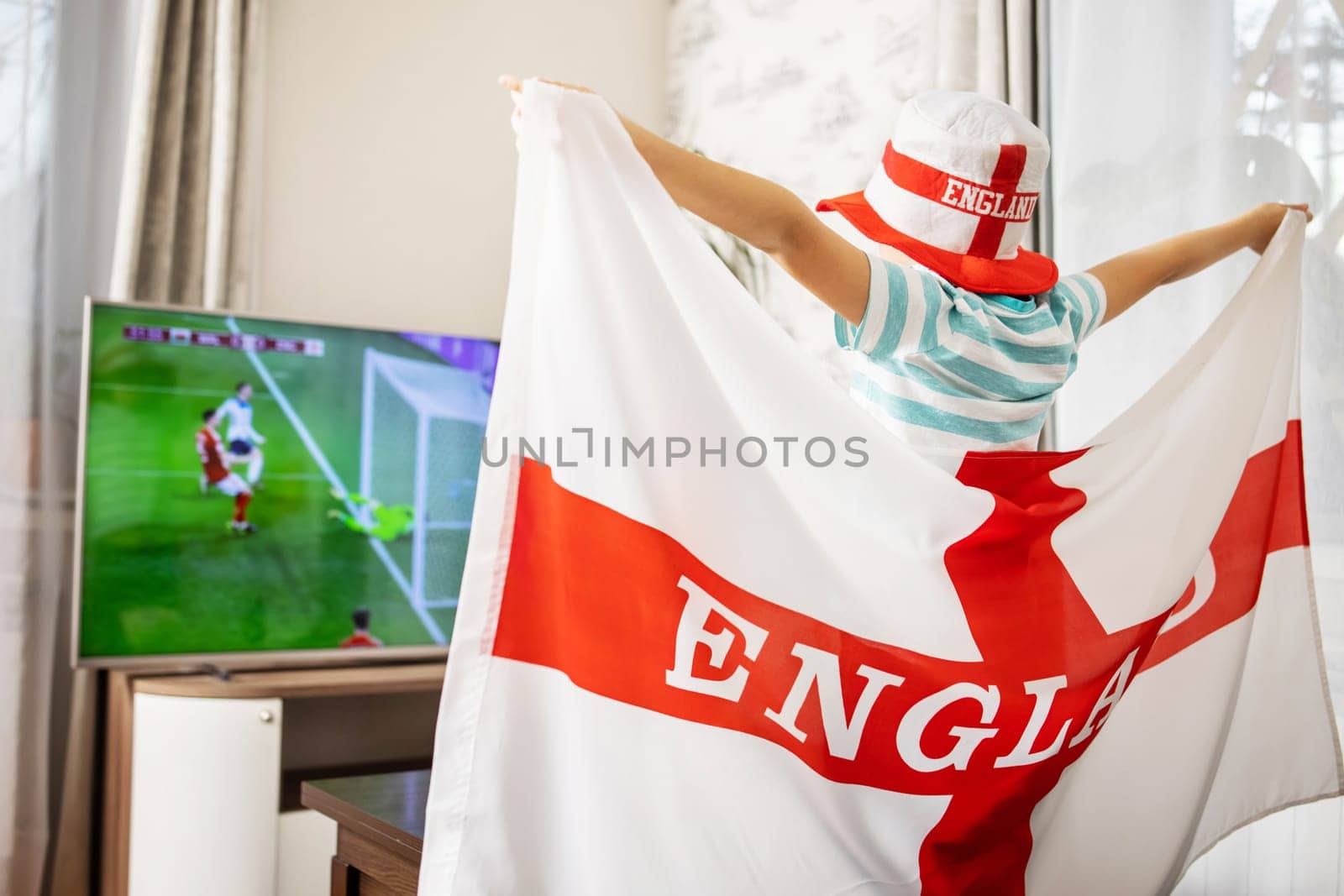 A boy with England flag watching soccer game on TV and supporting his national football team