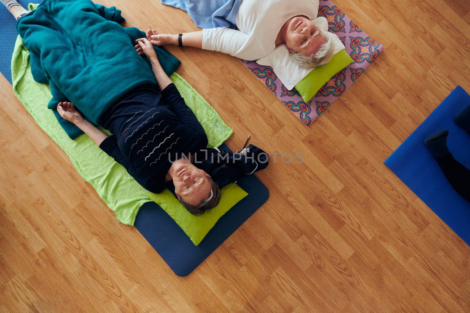 Top view of group of senior women engage in various yoga exercises, including neck, back, and leg stretches, under the guidance of a trainer in a sunlit space, promoting well-being and harmony by dotshock