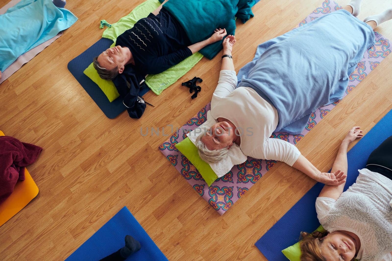 Top view of group of senior women engage in various yoga exercises, including neck, back, and leg stretches, under the guidance of a trainer in a sunlit space, promoting well-being and harmony by dotshock
