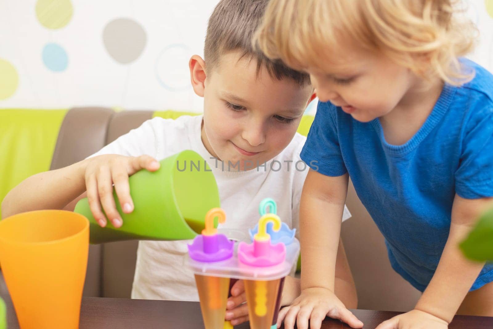 Two kids make ice cream from fruit juice on table at home.