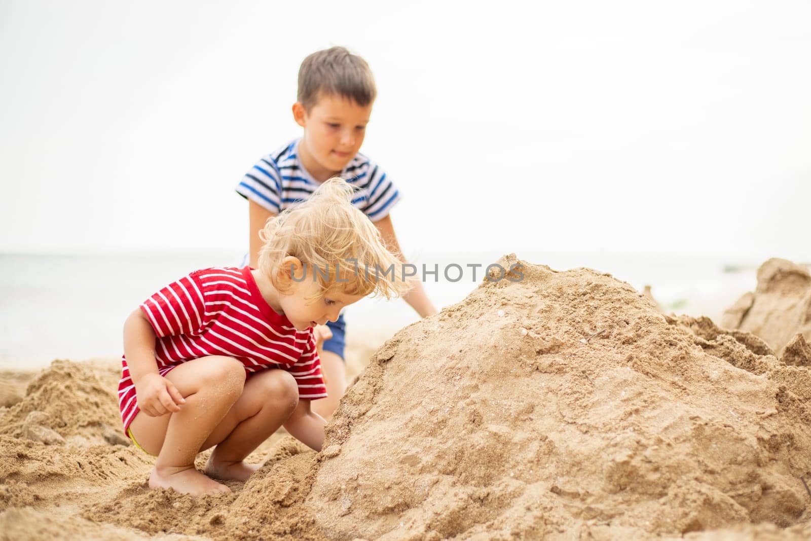 Two little boys playing on sandy beach. Cute kids building sandcastles on beach by andreyz
