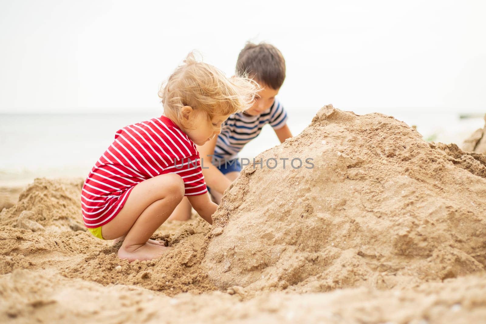 Two little boys playing on sandy beach. Cute kids building sandcastles on beach by andreyz