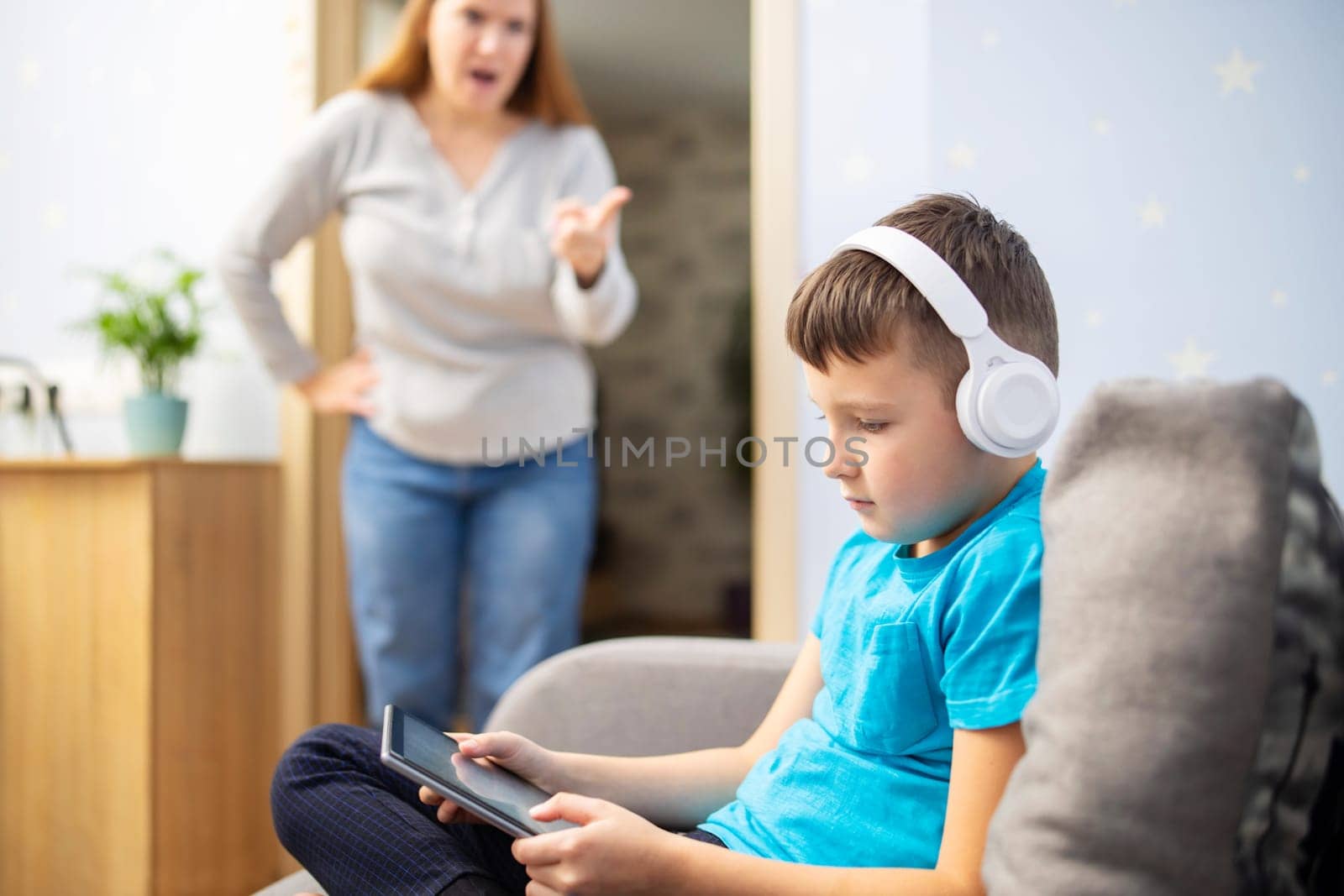Mother scolds her son. Boy uses tablet with headphones and ignores his mom by andreyz