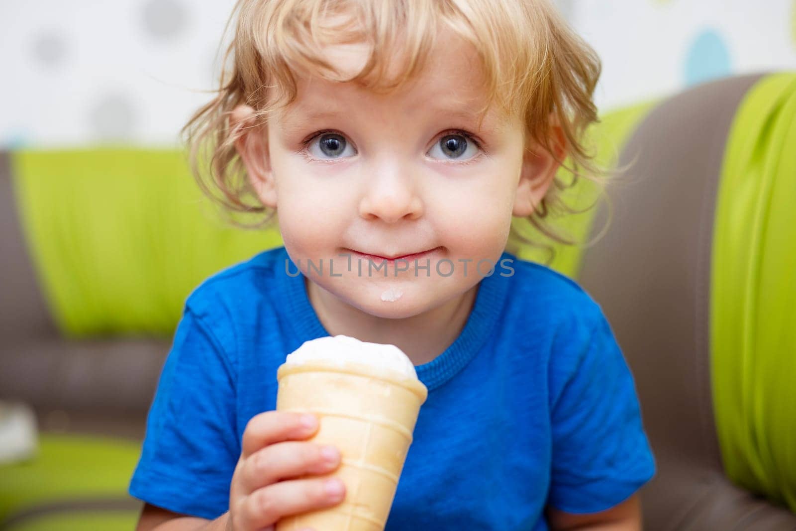 Happy little child in blue t-shirt eating ice cream at home.