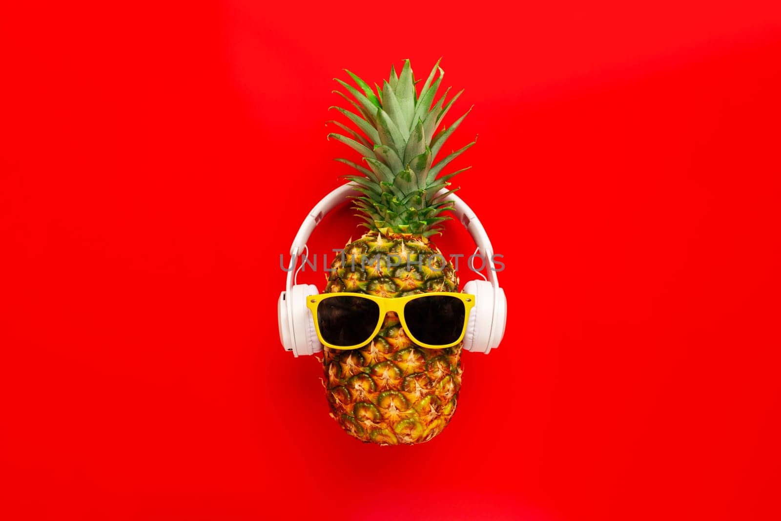 Ripe pineapple with sunglasses and headphones on red background by andreyz