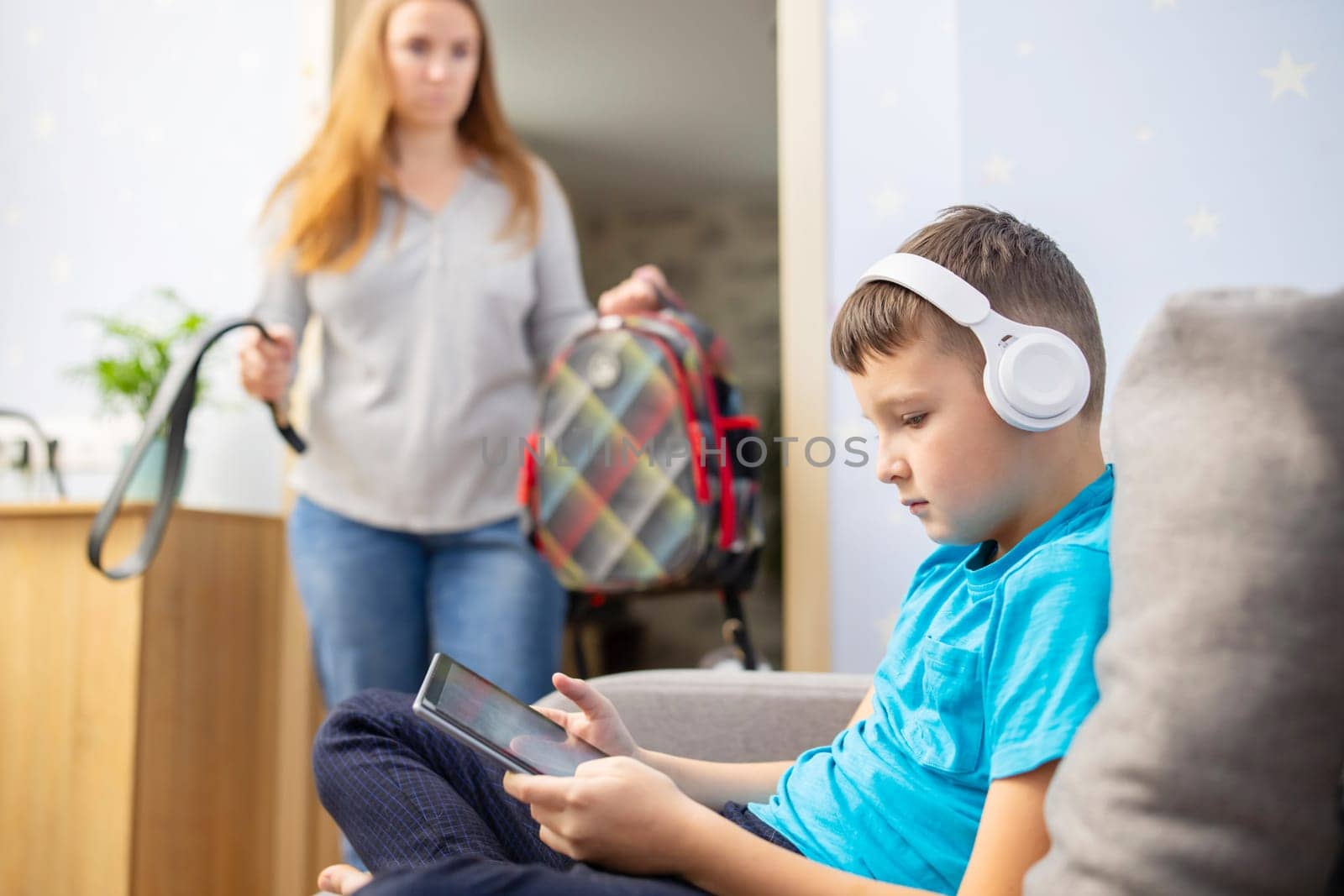 Mother scolds her son. Boy uses tablet computer with headphones and ignores his mom. Family relationships concept