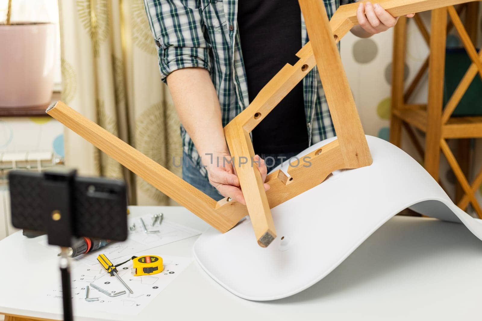 Handyman blogger shows assembling chair, shooting video instructions on smartphone . Man assembling furniture by yourself. Blog about carpentry