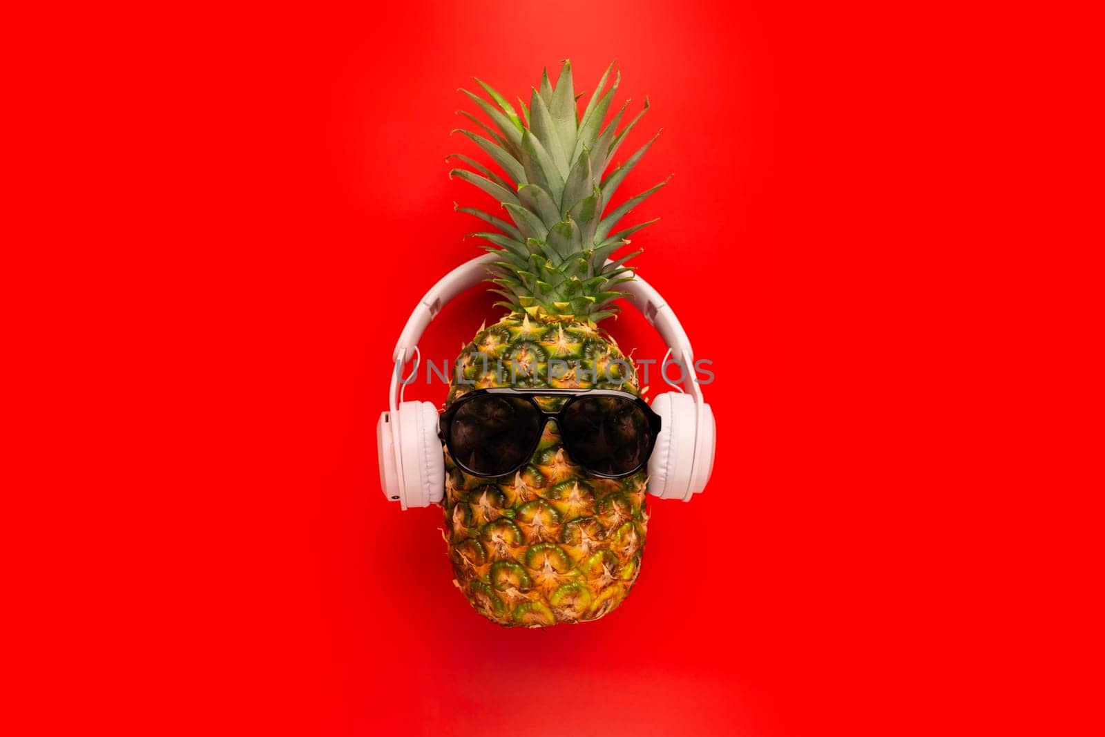 Ripe pineapple with sunglasses and headphones on red background by andreyz