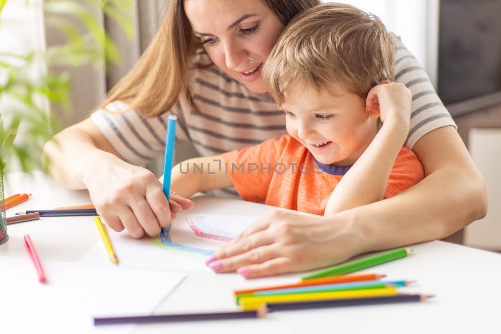 Mother and child drawing with pencils sitting at the desk at home. Happy family