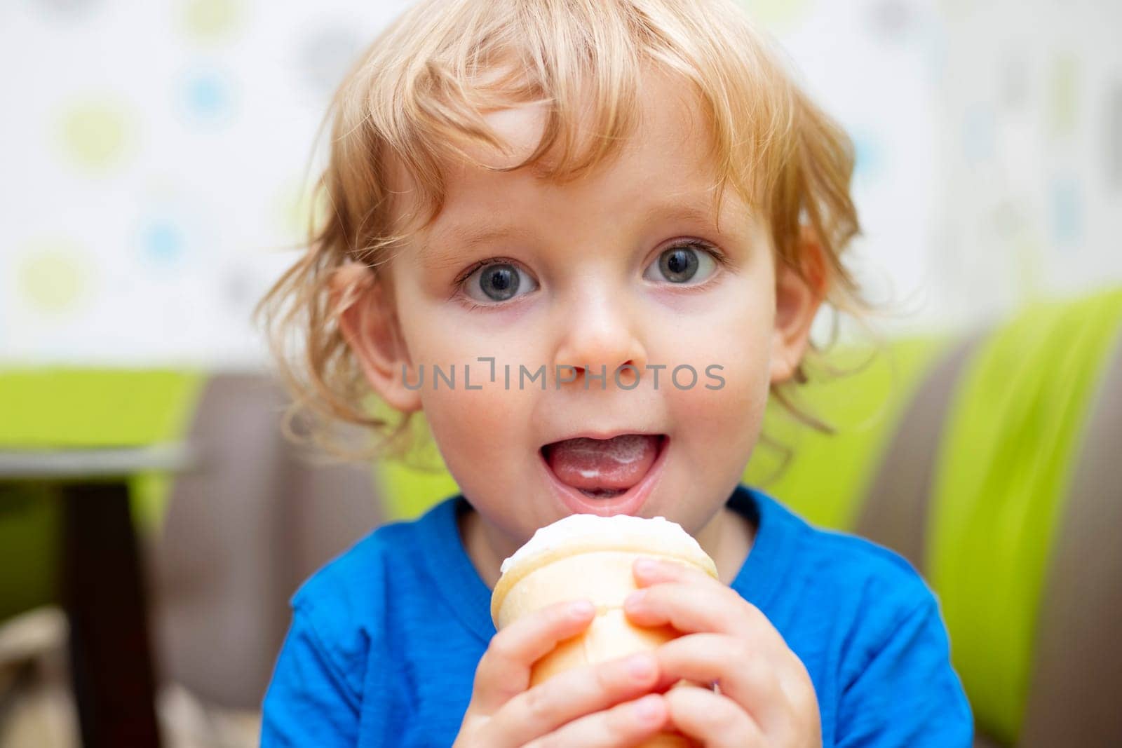 Happy little child in blue t-shirt eating ice cream at home.