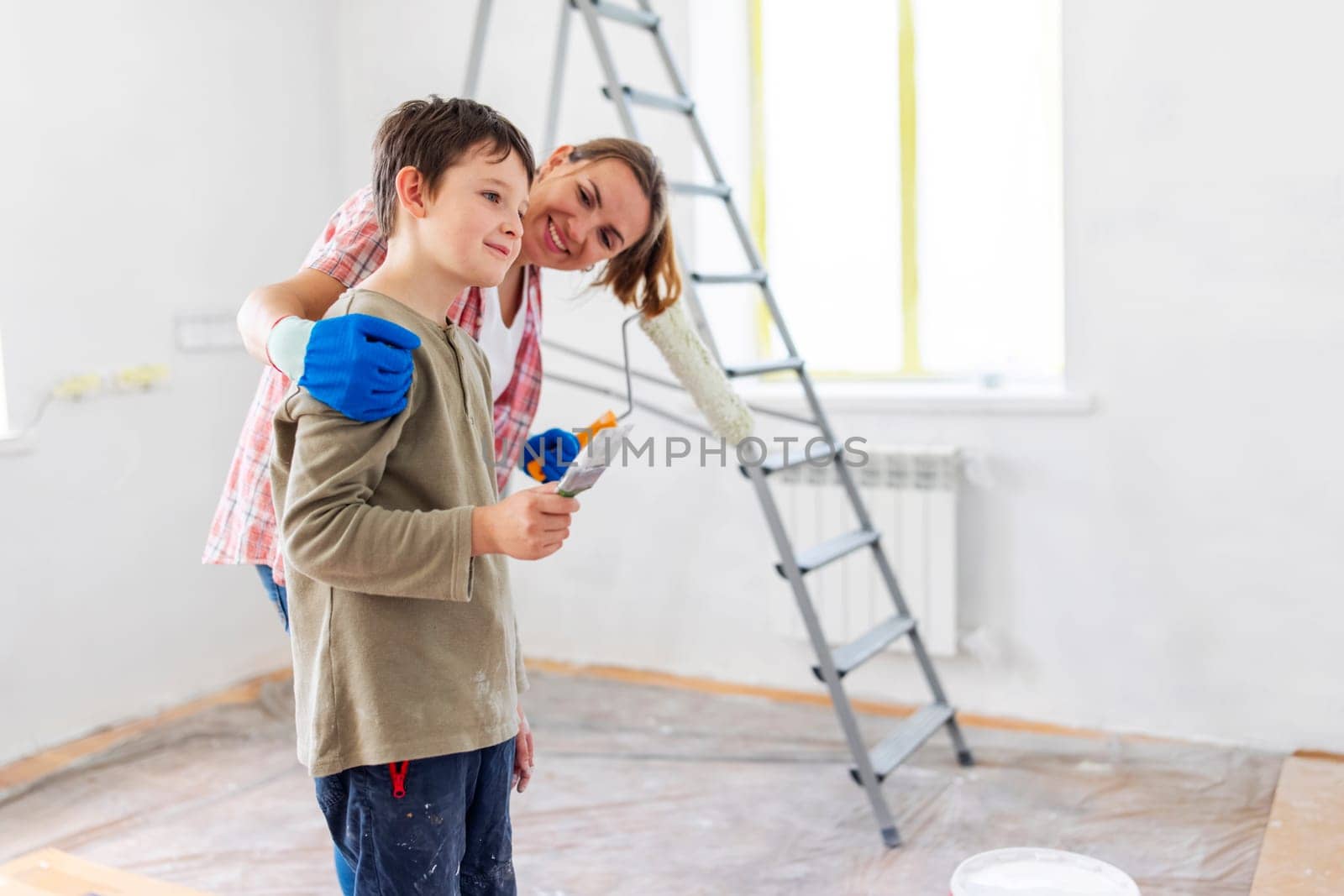 Happy family mother and child son paint the wall with paint using roller and brush. Repair in the apartment