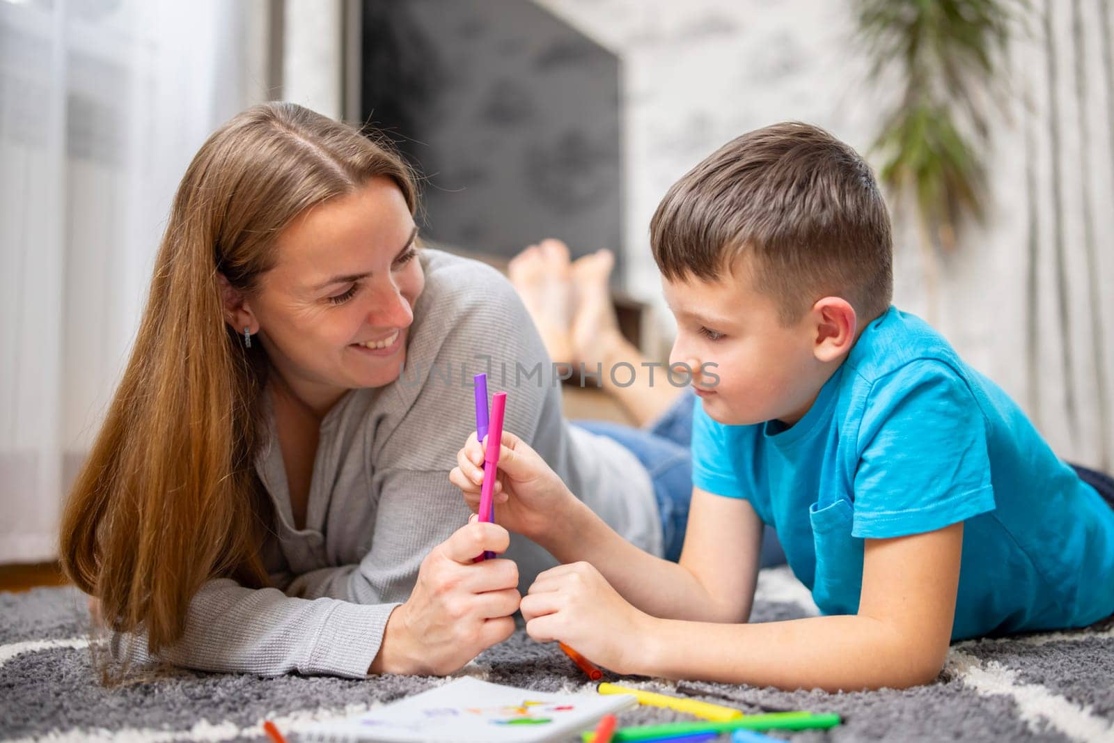 Happy family playing together at home on floor. Mother and her son painting together