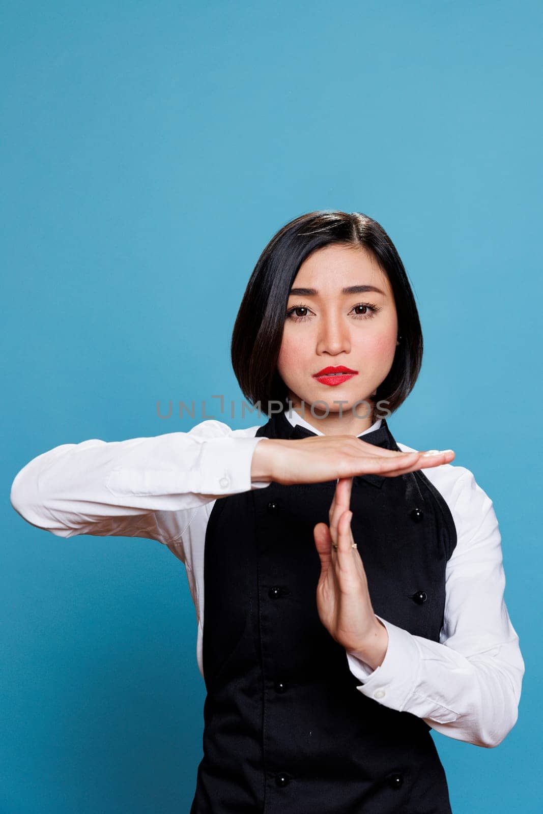 Serious asian waitress in uniform showing timeout sign with hands, asking to take break portrait. Young woman receptionist making interruption and pause gesture while looking at camera