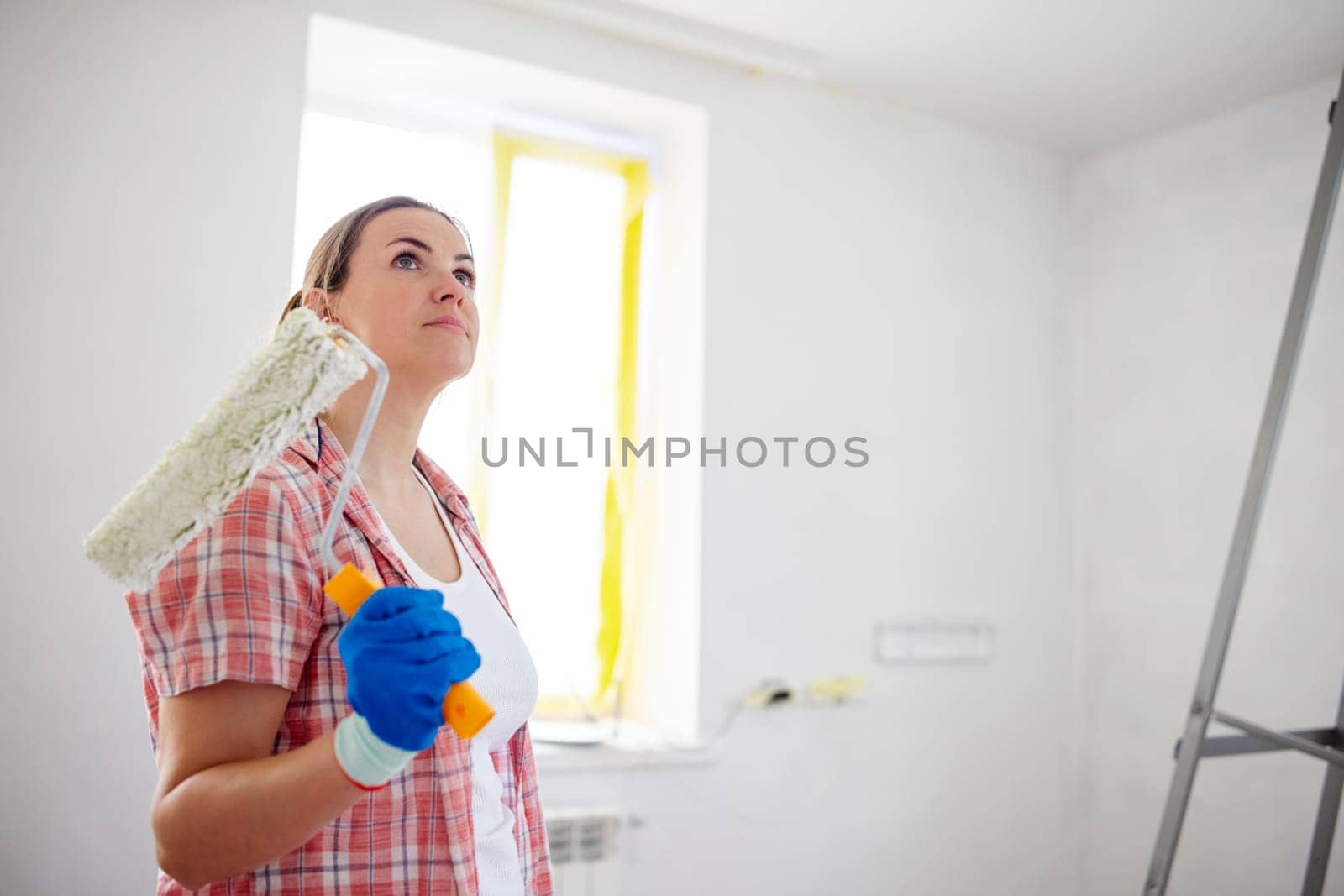 People renovation and home improvement. Positive satisfied woman holding dirty roller after painting walls in room