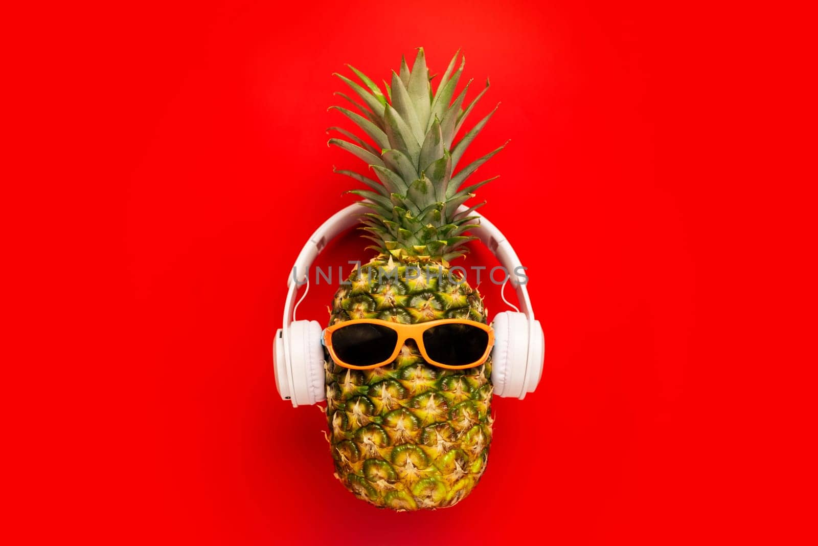 Ripe pineapple with sunglasses and headphones on red background. Copy space