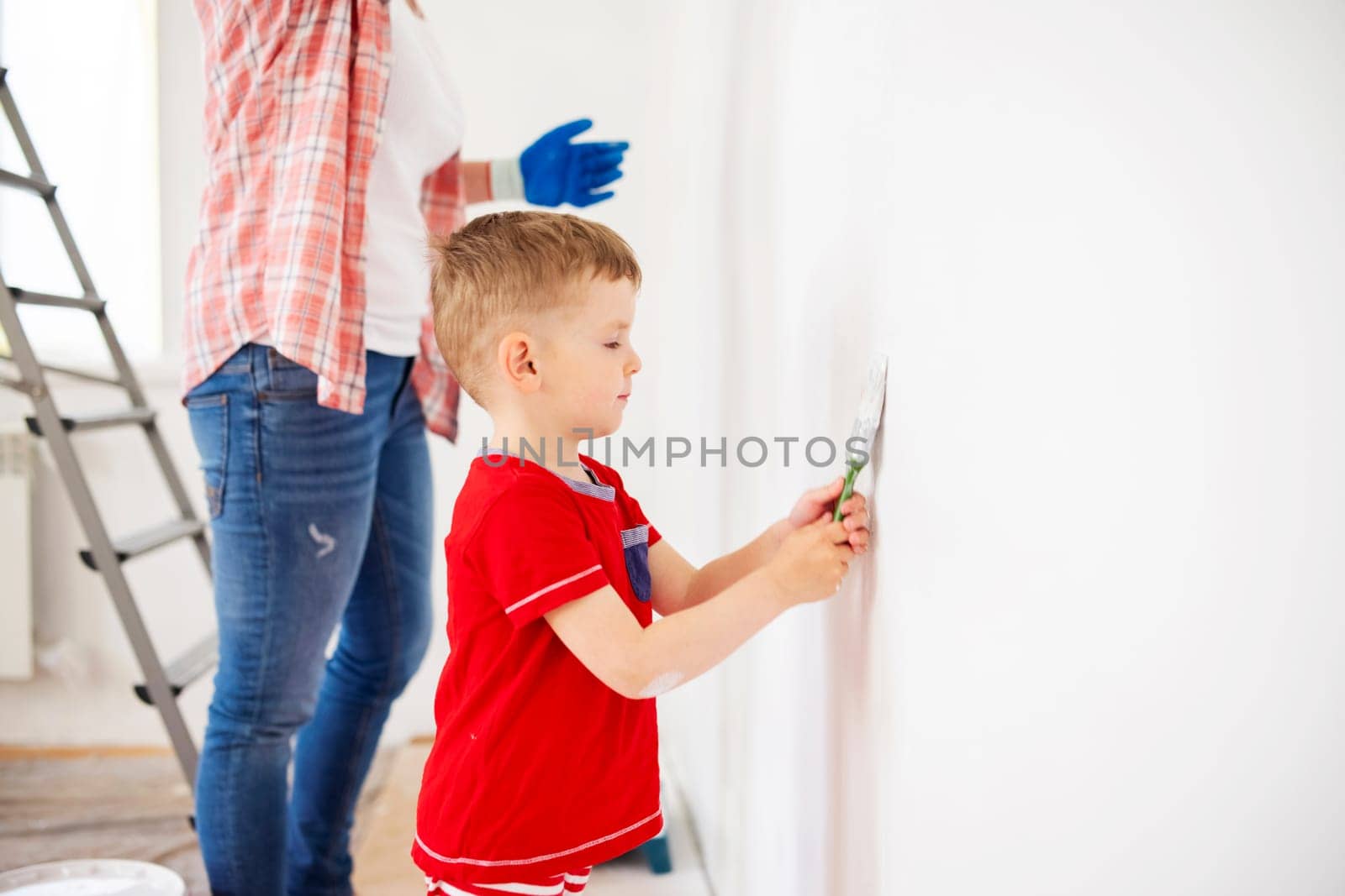 Happy family mother and child son paint the wall with paint using roller and brush. Repair in the apartment