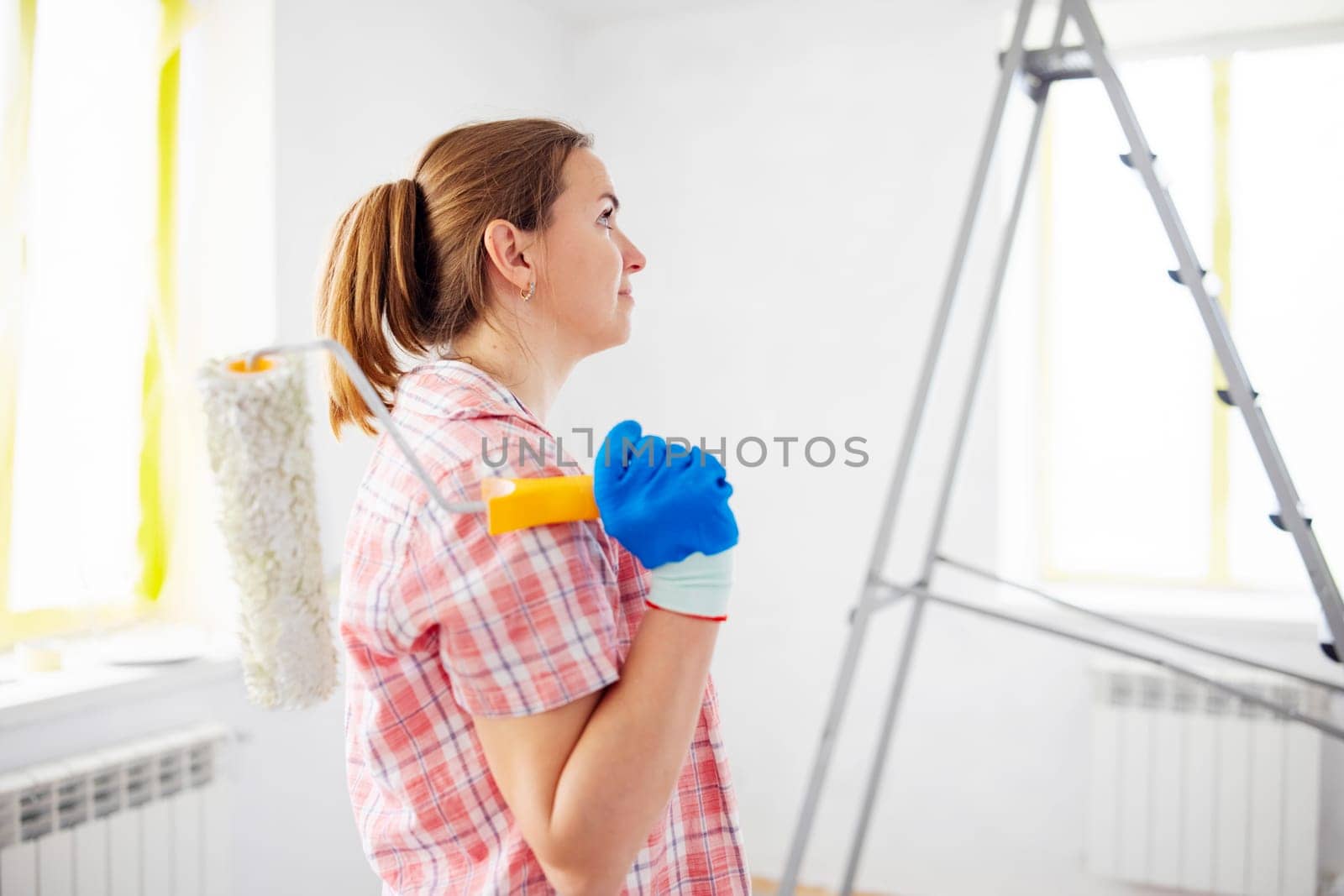 People renovation and home improvement. Positive satisfied woman holding dirty roller after painting walls in room