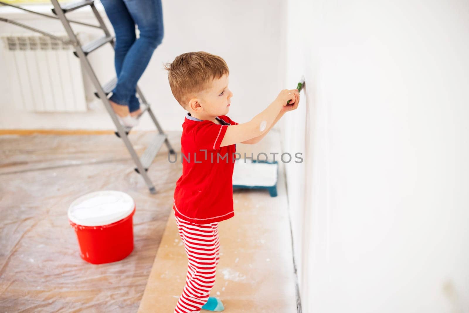 Happy family mother and child son paint the wall with paint using roller and brush. Repair in the apartment