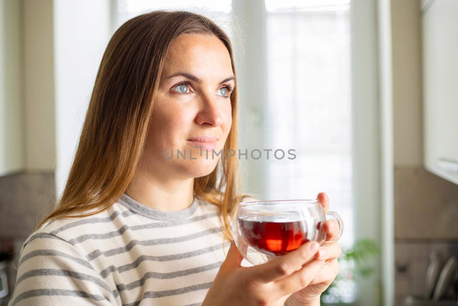 Woman holding a cup of hot tea in the morning. Looking out the window and drinking tea. Good morning with tea