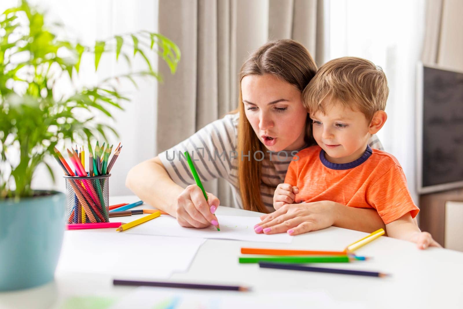 Mother and child drawing with pencils sitting at the desk at home by andreyz