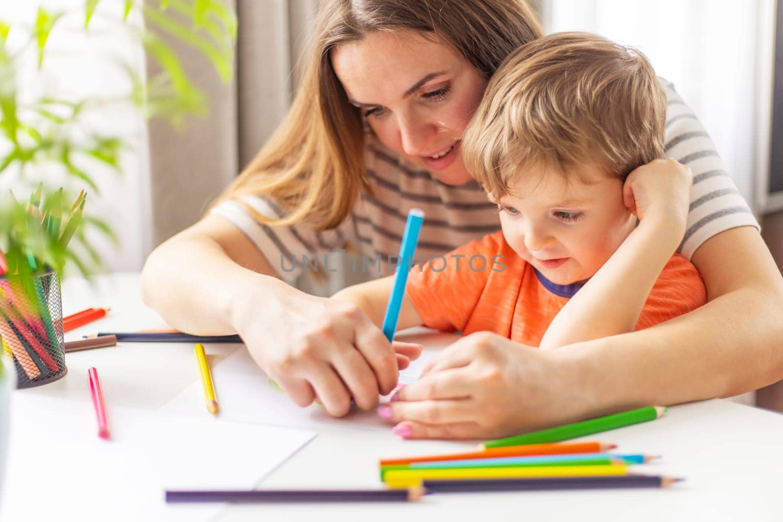 Mother and child drawing with pencils sitting at the desk at home. Happy family