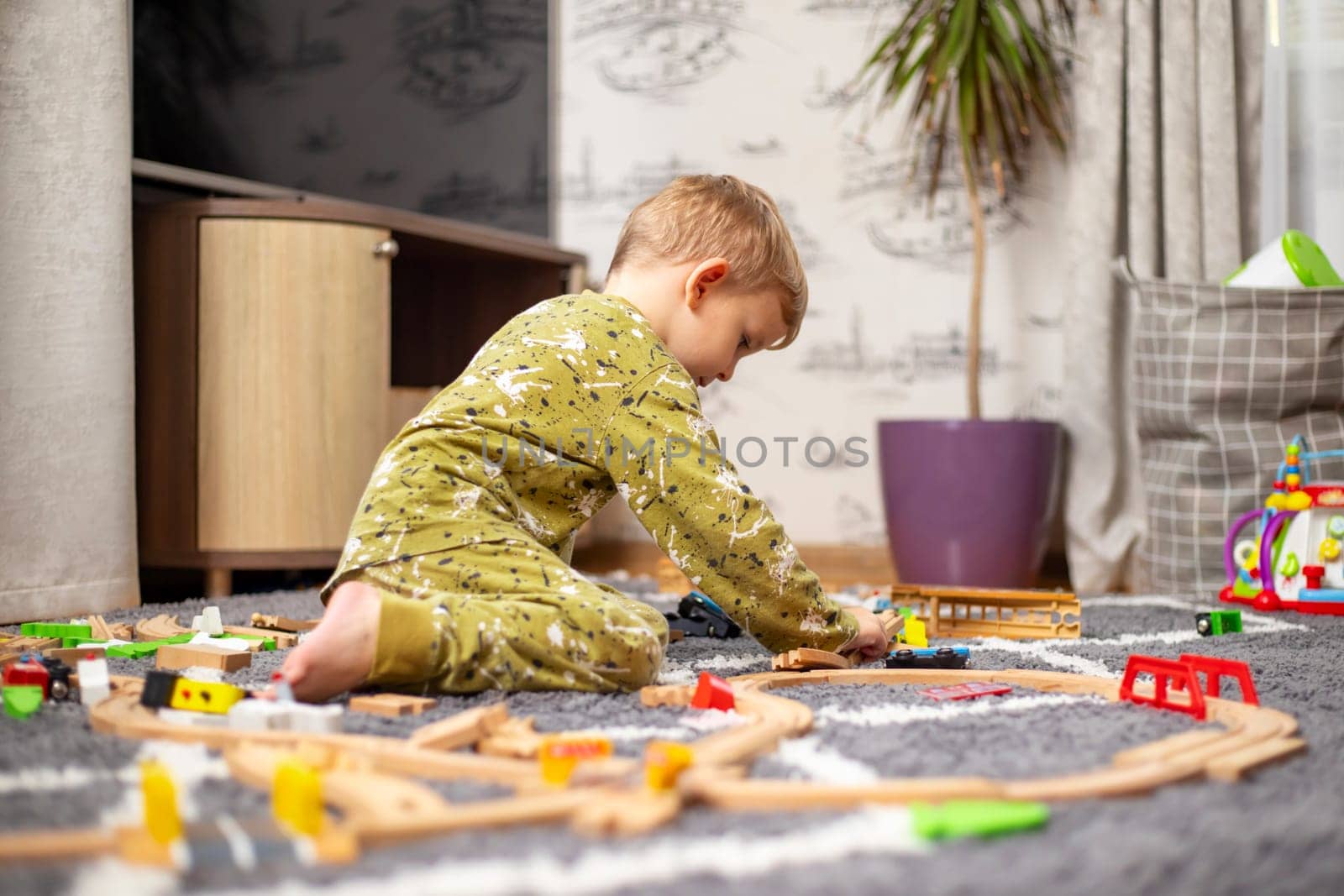 Child playing with developmental toys. Baby playing with toy railroad, trains and cars on the floor. Children at home or in kindergarten