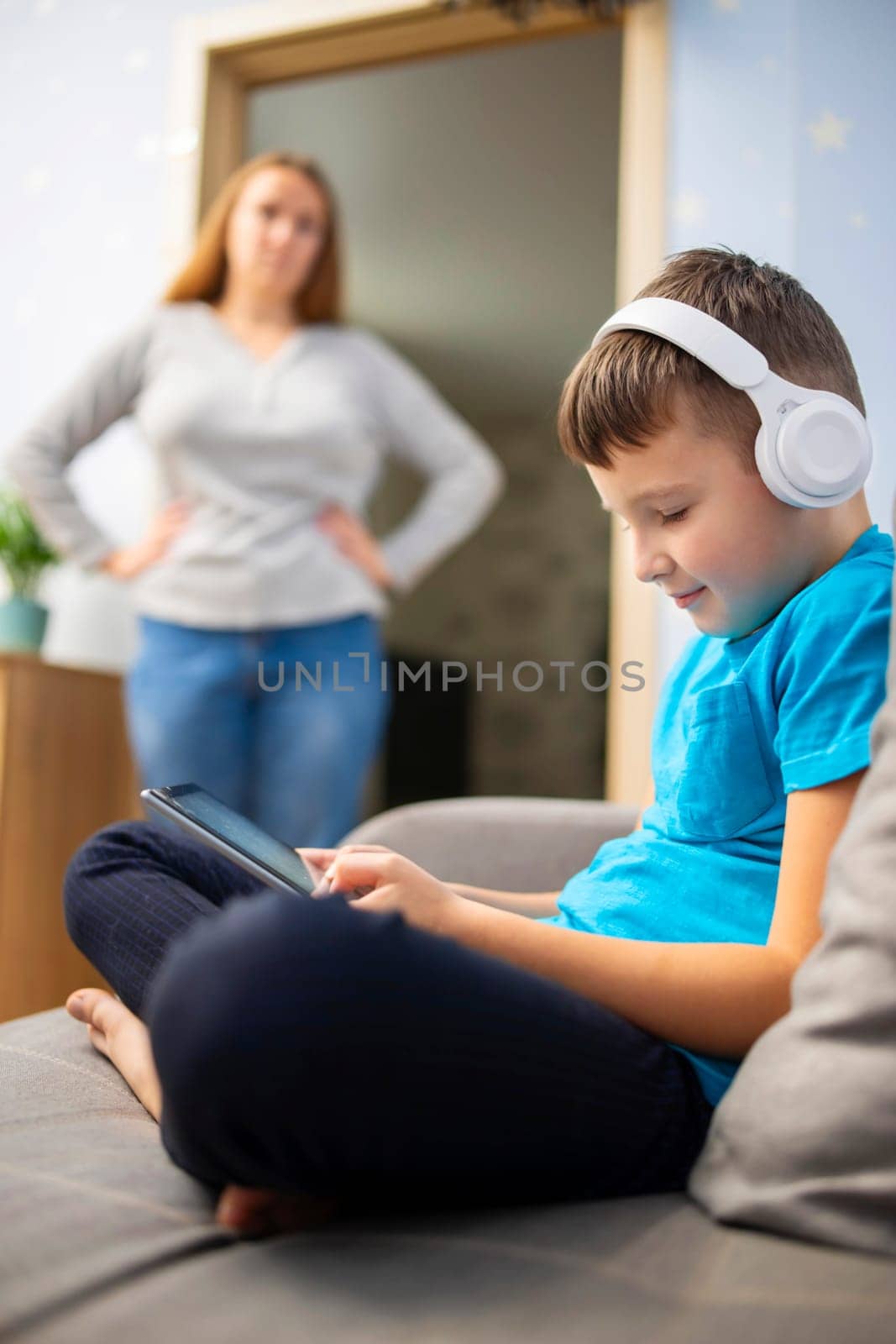 Mother scolds her son. Boy uses tablet with headphones and ignores his mom by andreyz