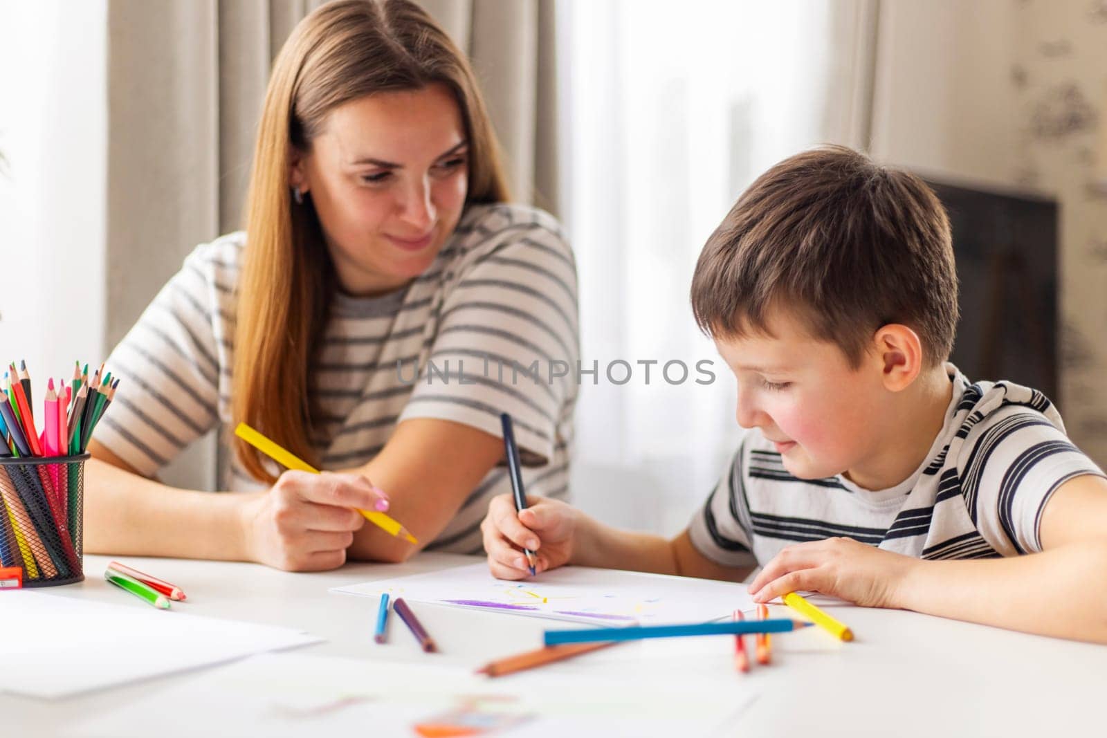 Mother and child drawing with pencils sitting at the desk at home by andreyz