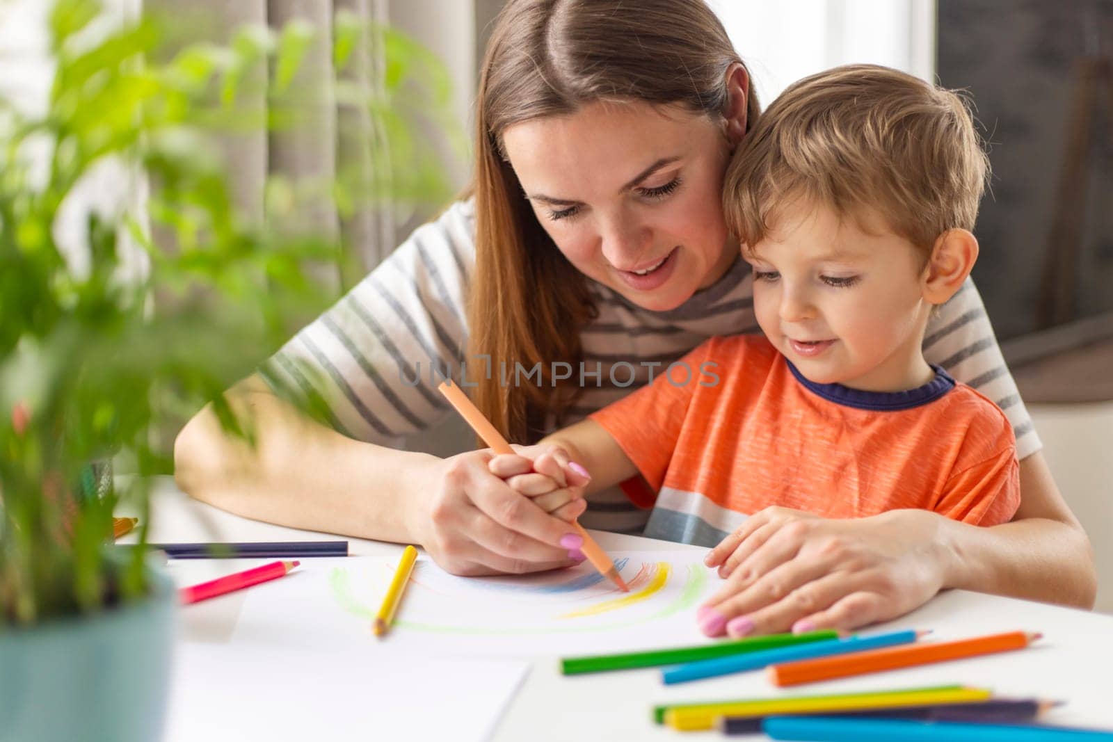 Mother and child drawing with pencils sitting at the desk at home. Happy family