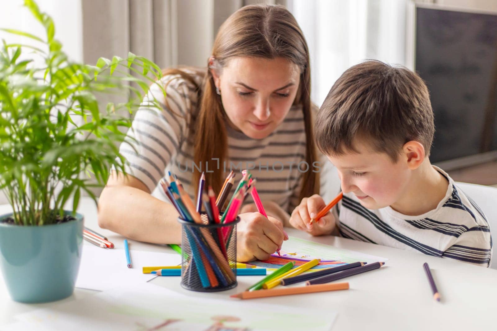 Mother and child drawing with pencils sitting at the desk at home by andreyz