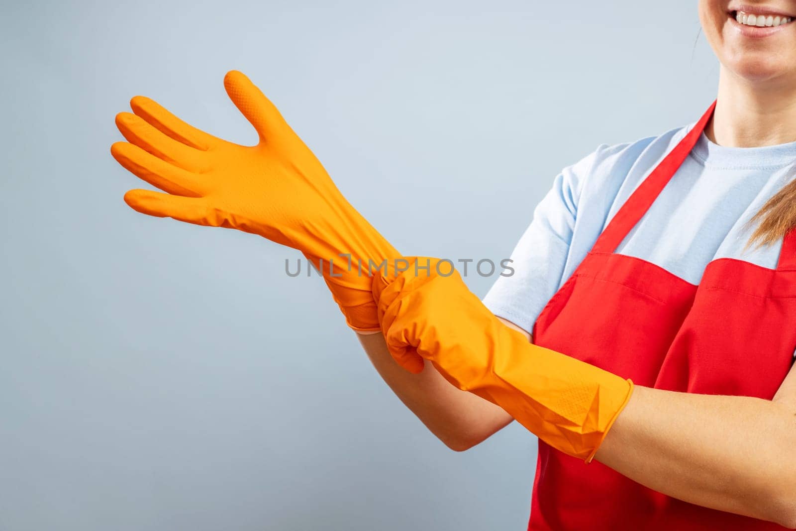 A woman in red apron putting on protective gloves on blue background. Clean and remove germs and dirt in the house