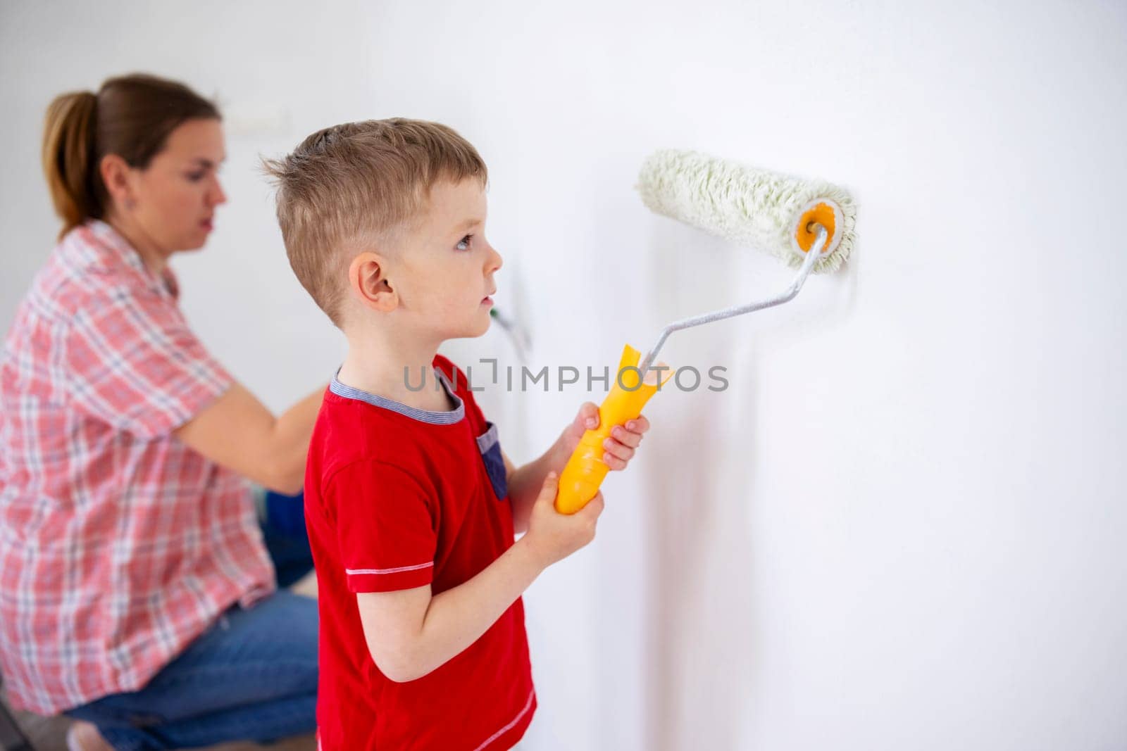 Happy family mother and child son paint the wall with paint using roller and brush. Repair in the apartment